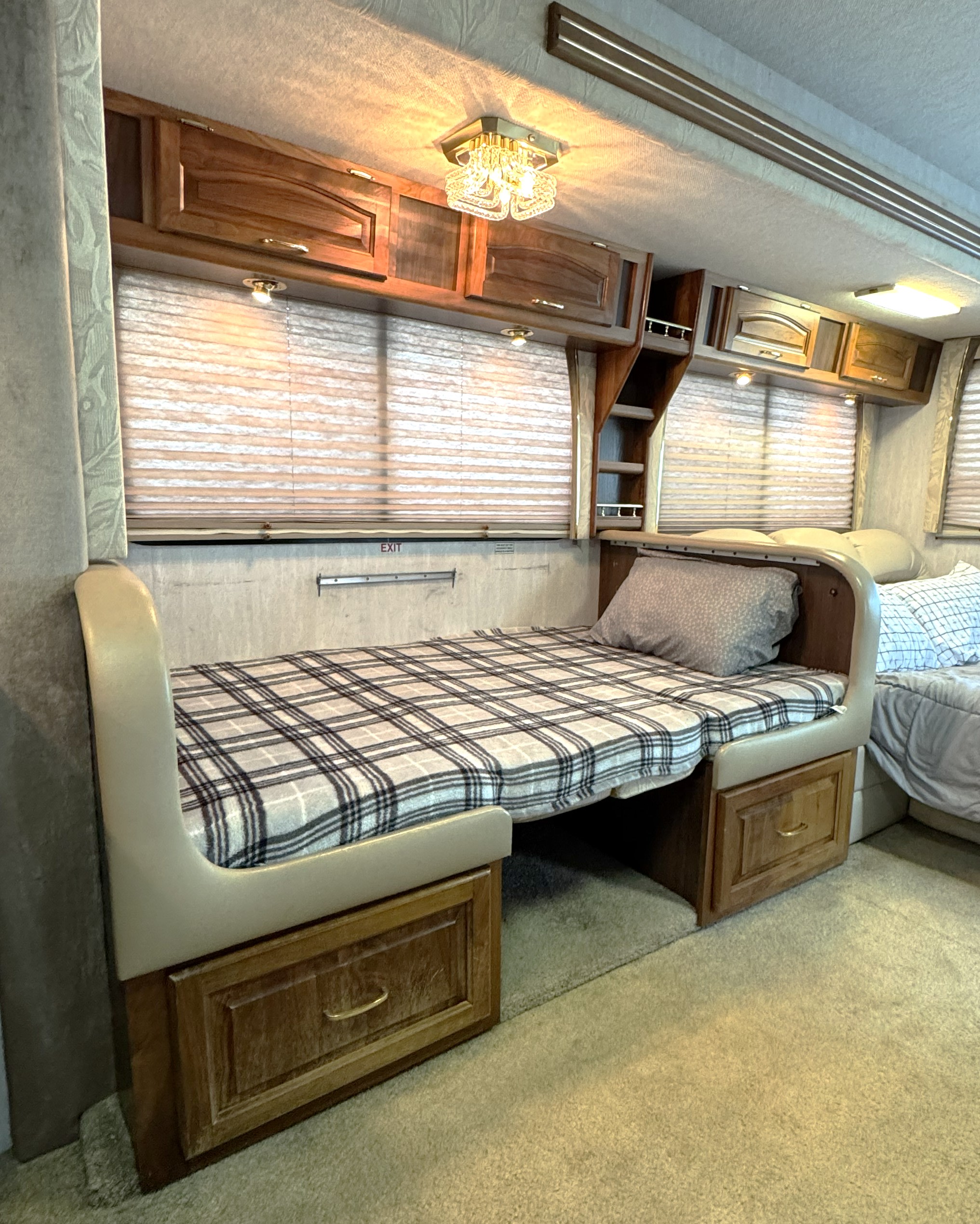Cozy RV rental interior with a bed, plaid blanket, wooden cabinets, and window blinds.. National Tradewinds 1998