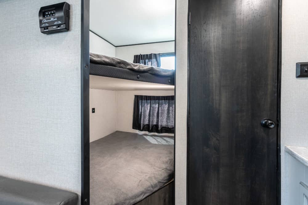 This RV rental features stacked bunk beds with window curtains, a thermostat, and a dark door, offering a compact sleeping space.. Starcraft Autumn Ridge 2022