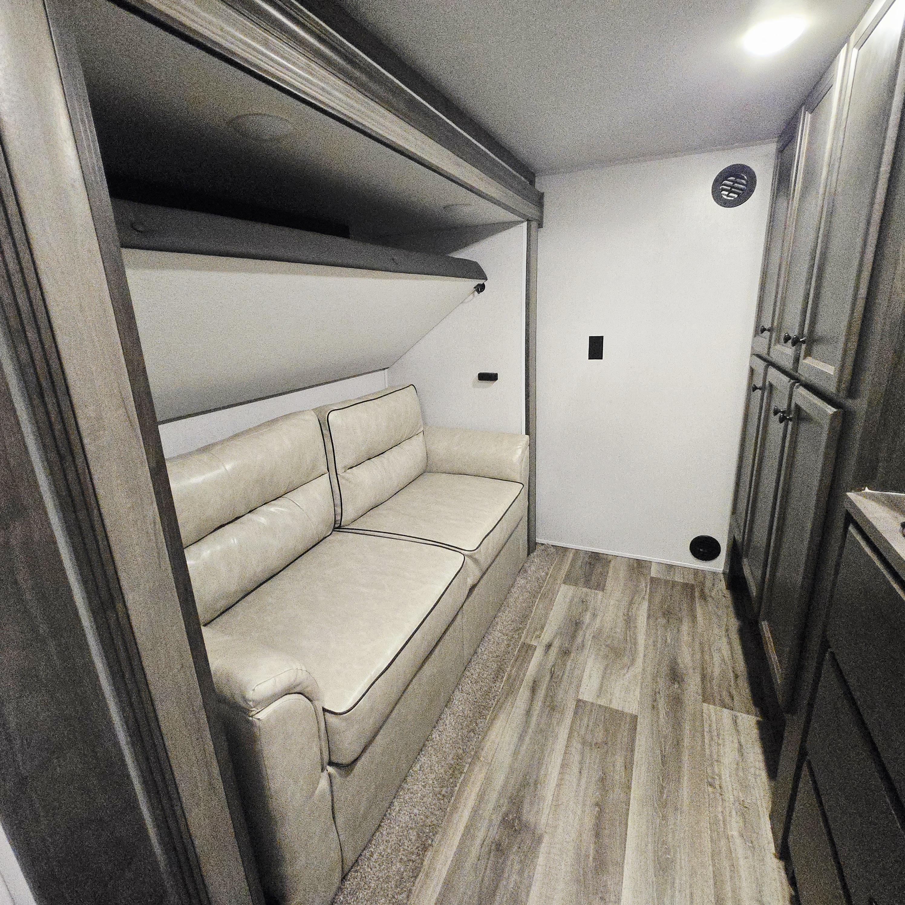 Cozy RV rental interior featuring a cream sofa, a pull-down bunk bed, wood-grain cabinets, and modern flooring.. Forest River Cardinal Limited 2021