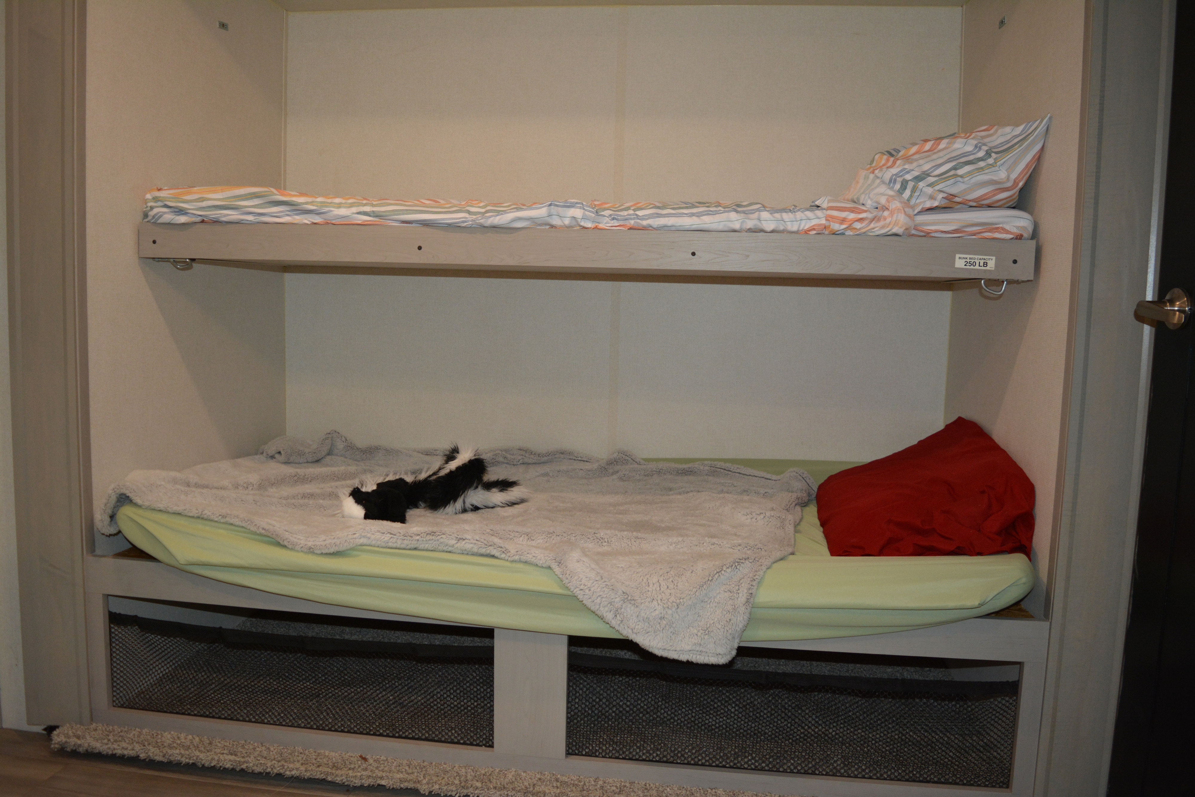 Cozy RV rental bunk beds. Top bunk has striped bedding; bottom has a gray blanket, red pillow, and a plush skunk toy.. Forest River Tracer 2023
