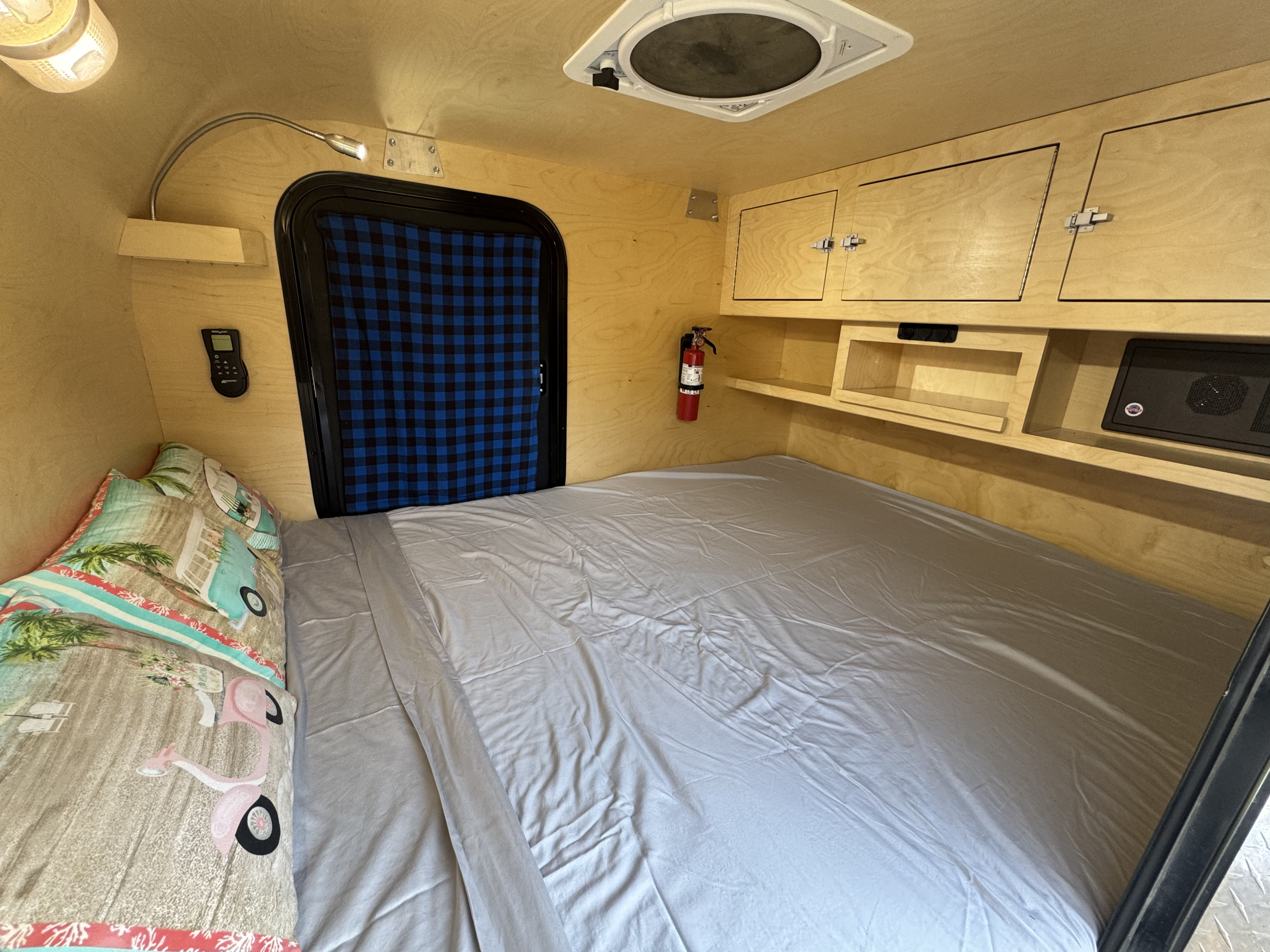 Cozy rv rental interior featuring a bed with light gray sheets, wood walls, overhead cabinets, shelves, and a fan.. Gnome Homes Inc. Backcountry 2020