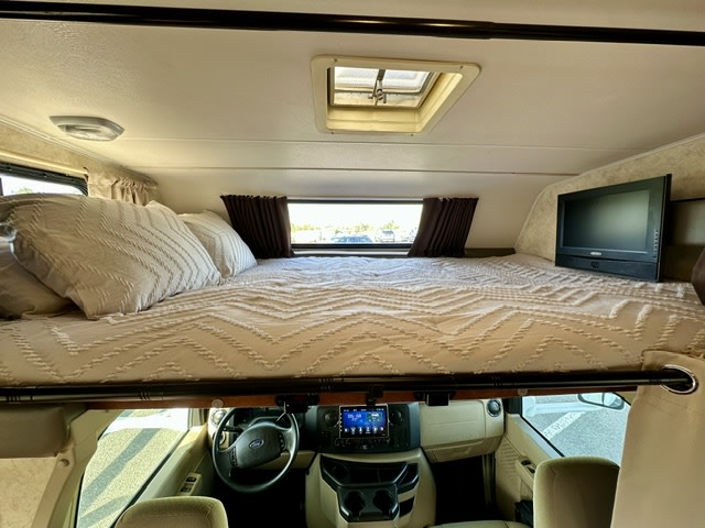 Experience comfort in this RV rental! View of the cab-over bunk bed with a TV, pillows, and the driver's cockpit below.. Coachmen Freelander 2011