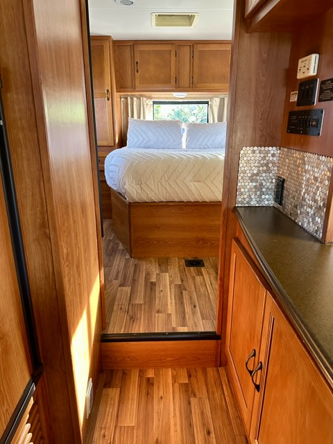 RV rental interior featuring a cozy bedroom with wood cabinetry, crisp white bedding, and a hallway with a tiled counter.. Coachmen Freelander 2011