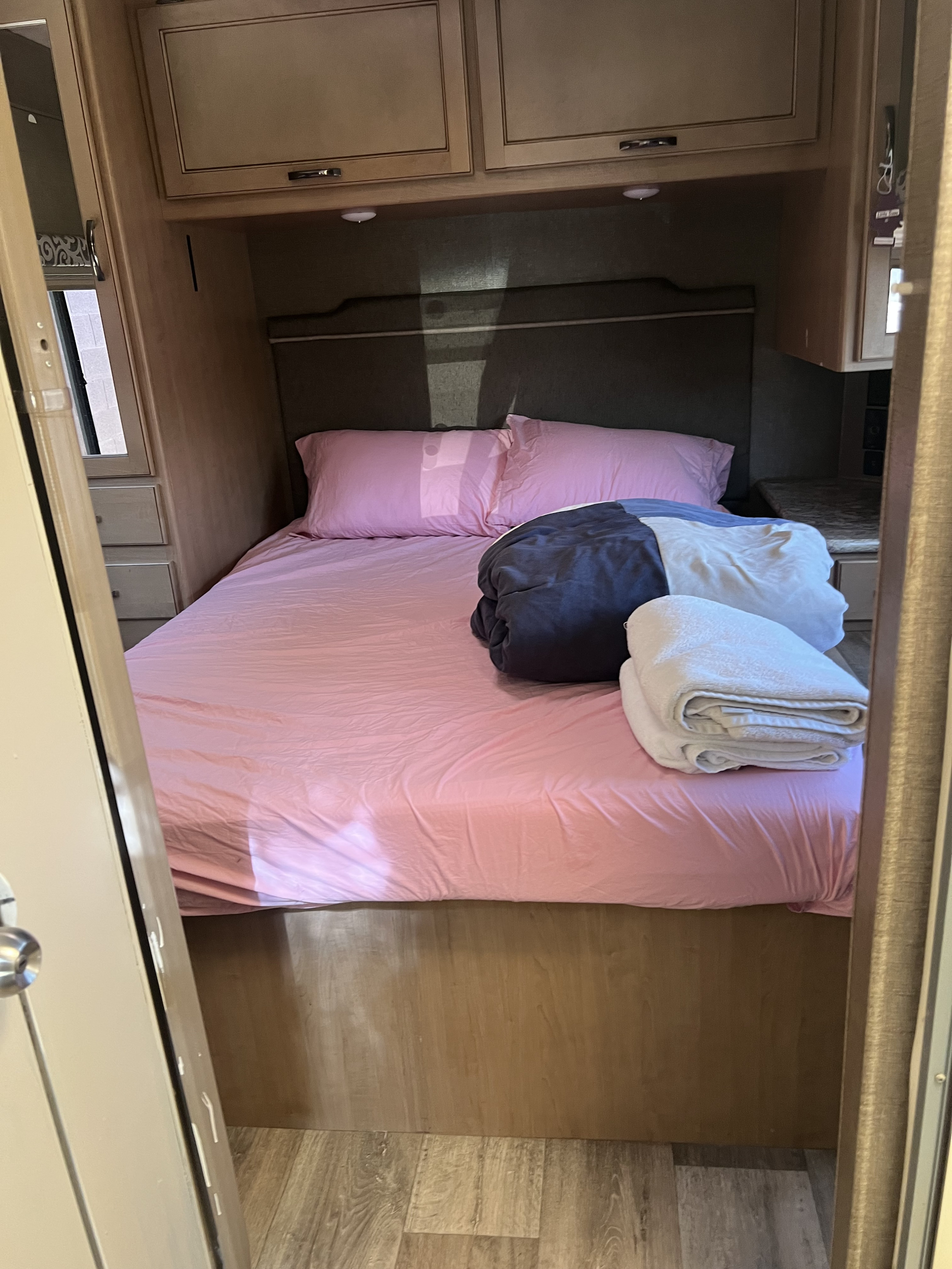A comfortable pink bed in a compact RV rental bedroom with overhead cabinets & fresh towels.. Thor Four Winds 2019