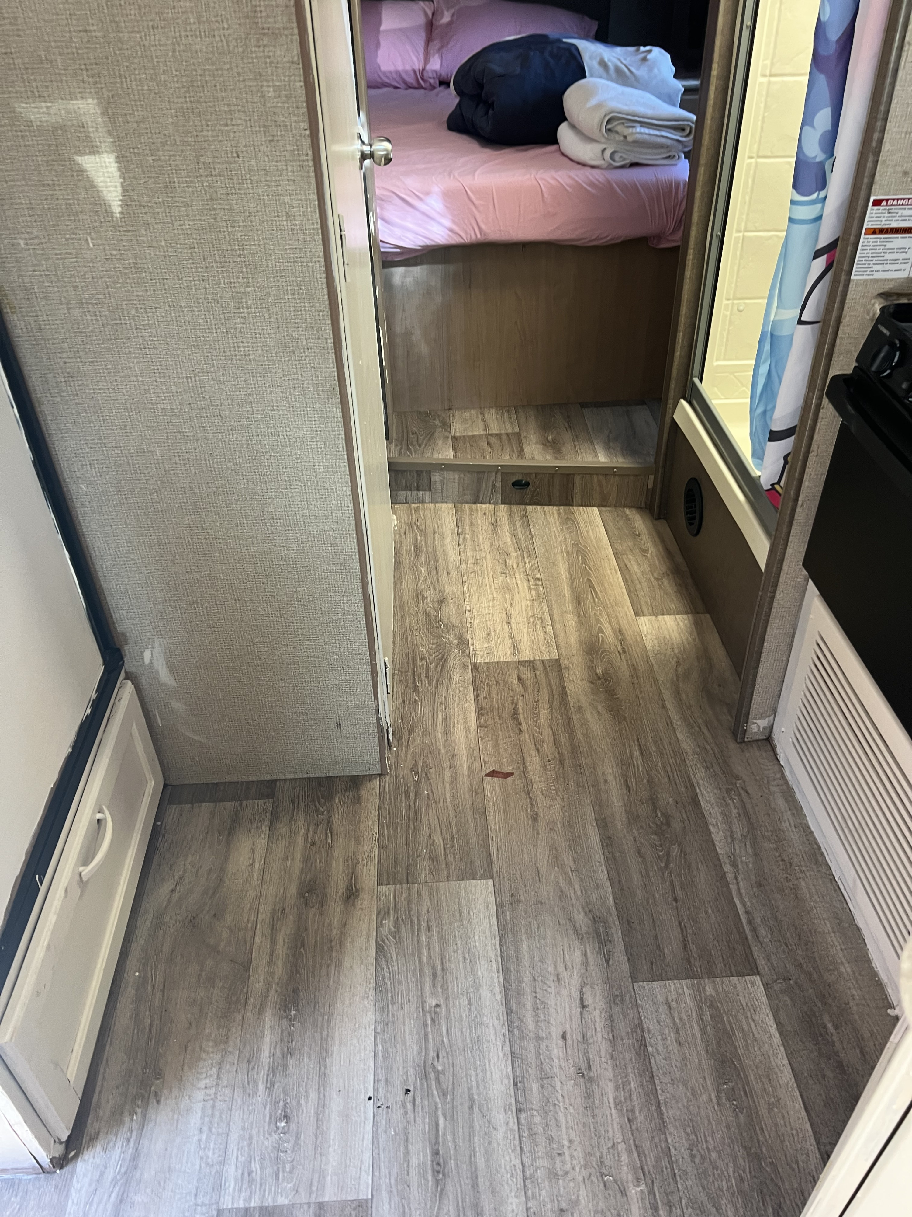 Inside an RV rental: view of the hallway with wood-look flooring leading to a compact bed area and a shower with a patterned curtain.. Thor Four Winds 2019