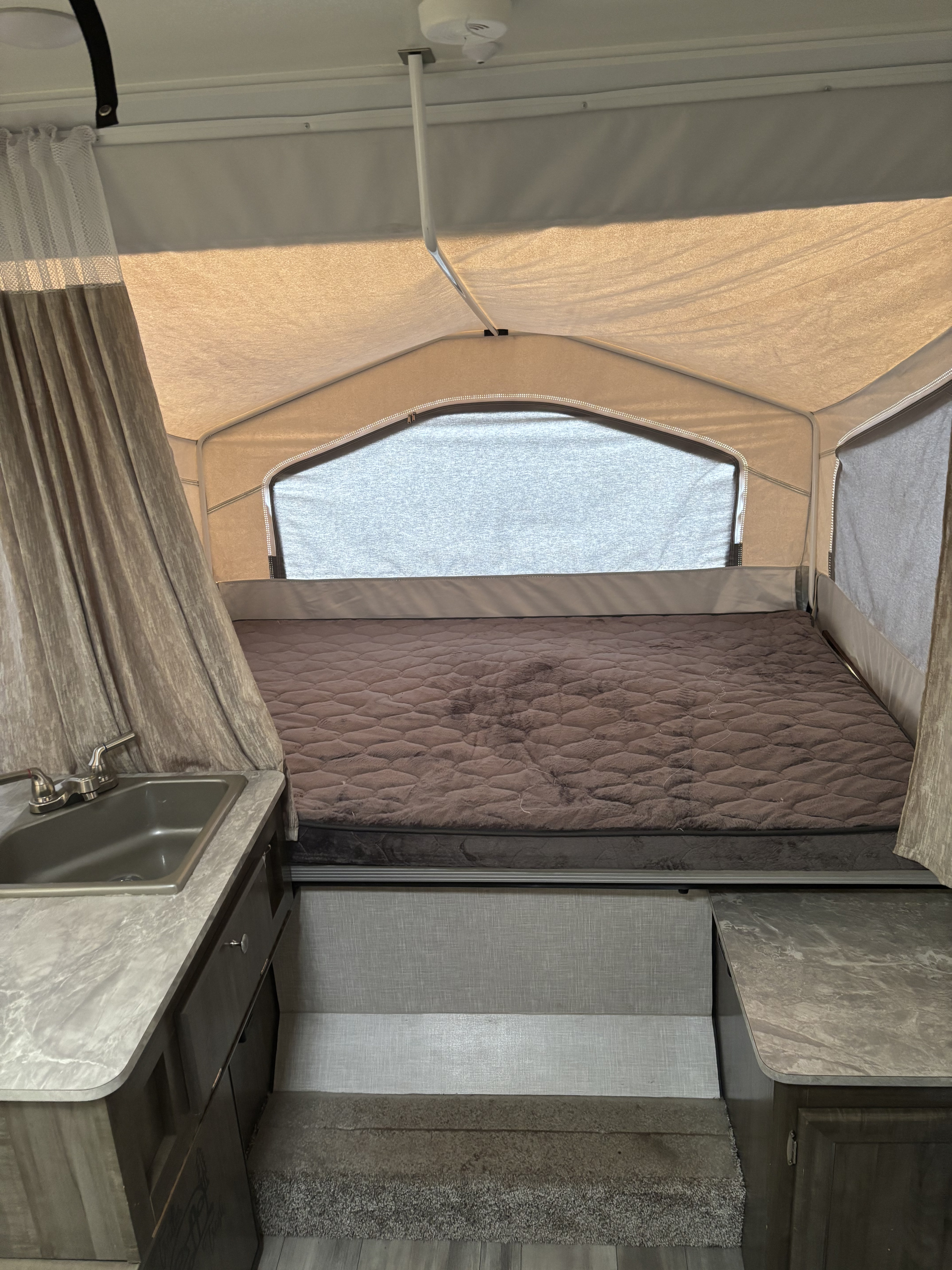 Interior of an rv rental pop-up camper with a large quilted bed, counter with sink, and fabric tenting for a cozy camping experience.. Rockwood 4X4CFM219ND314488 2022