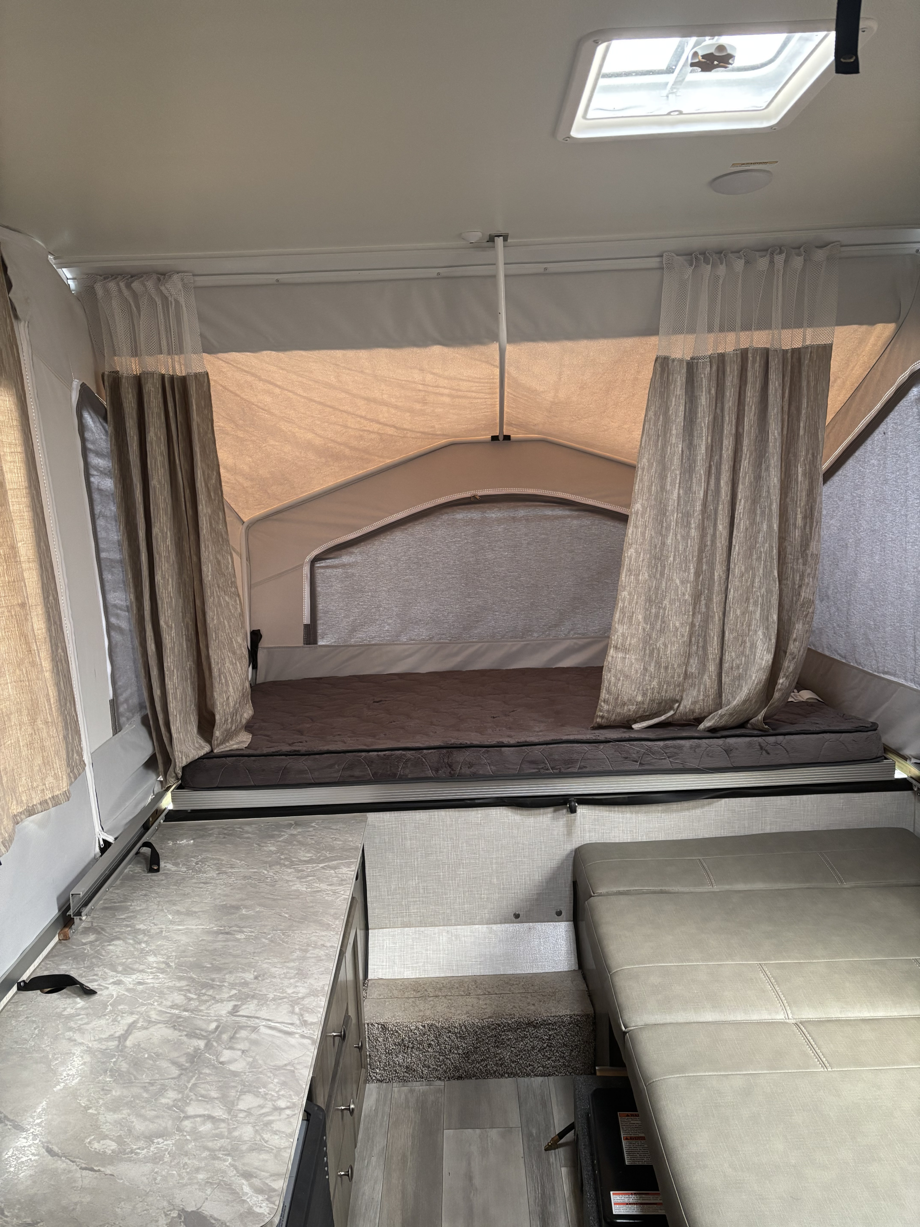 Inside an RV rental pop-up camper, featuring a cozy bed, patterned curtains, sleek counter, and plush seating.. Rockwood 4X4CFM219ND314488 2022