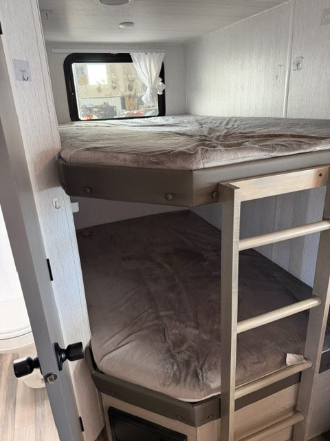 Cozy RV rental interior featuring bunk beds, a window, and an access ladder. Ideal for family travel accommodations.. Forest River EVO Lite 2025