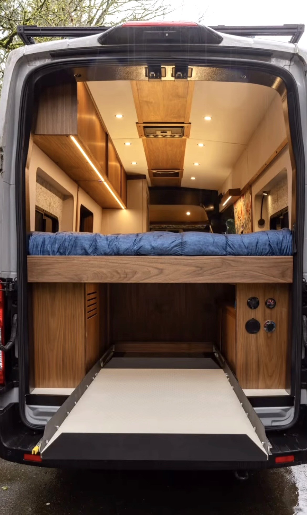 Explore this custom RV rental's cozy interior, featuring an elevated bed, ample storage, and a handy pull-out tray.. Ford Custom Transit 2024
