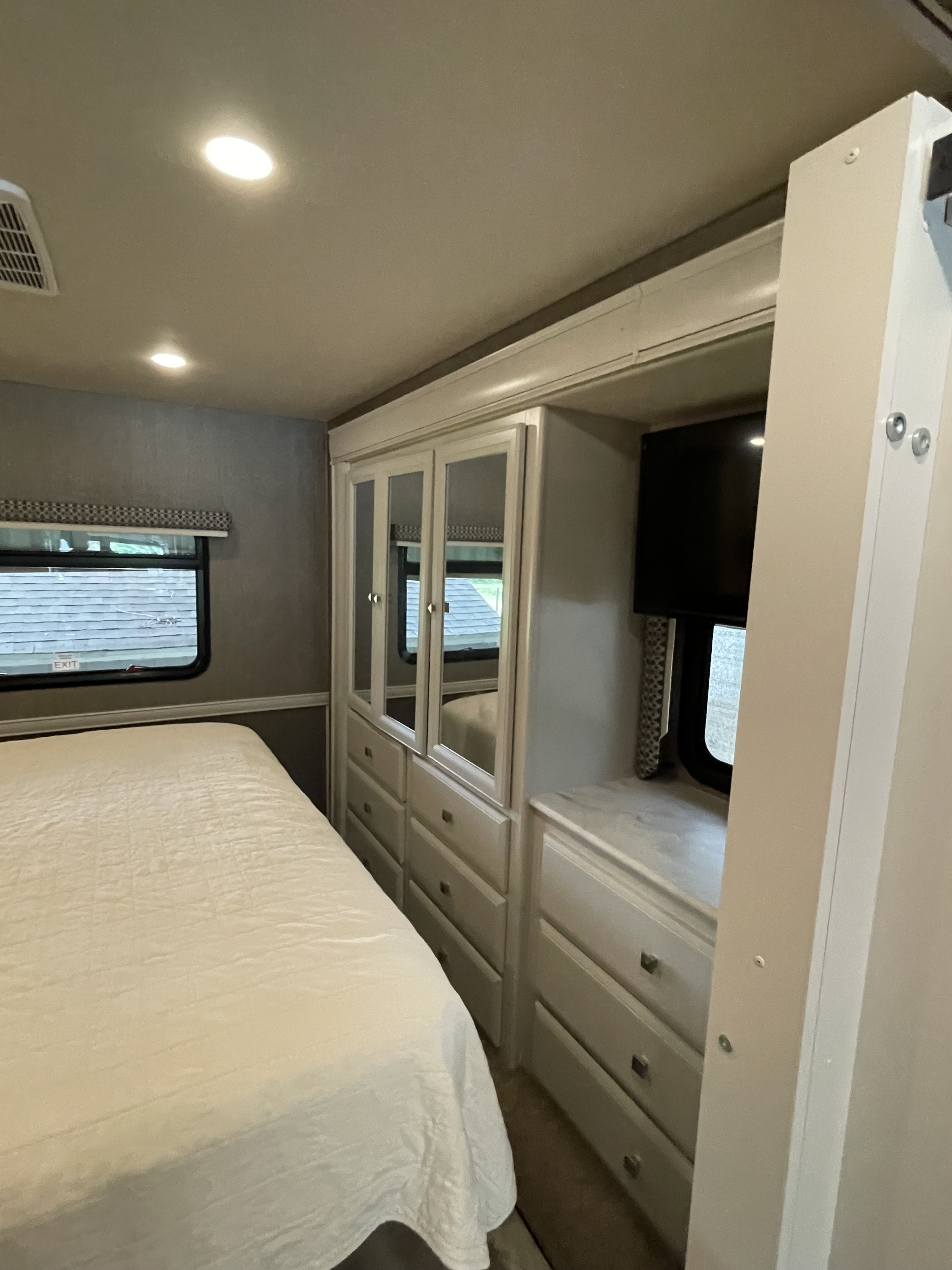 Cozy RV rental bedroom featuring a comfortable bed, window, and built-in storage with mirrored doors and a TV.. Holiday Rambler Admiral 2021
