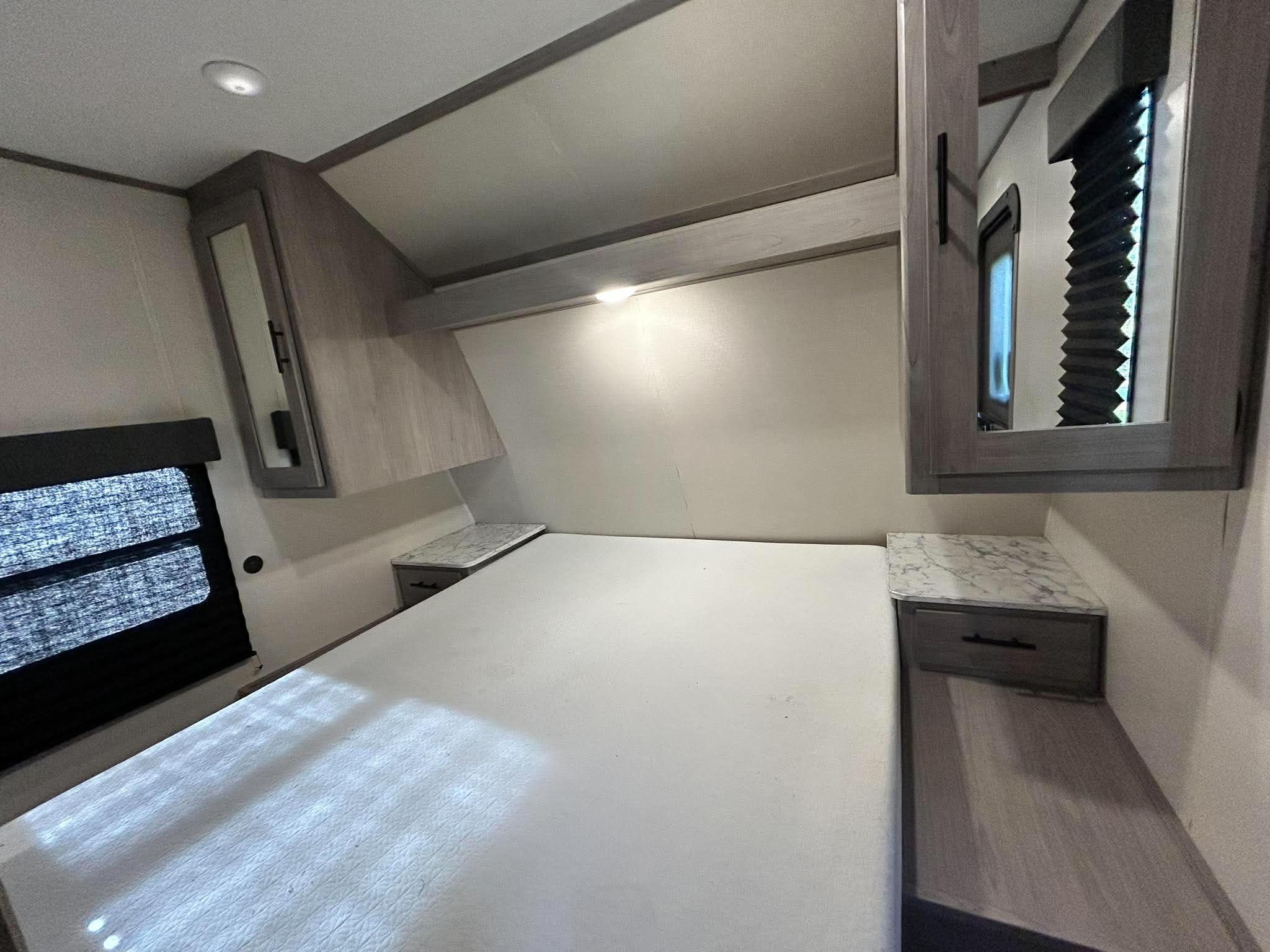 RV rental bedroom: Modern design with a large bed, built-in nightstands, overhead cabinets, and a window with dark blinds.. Other Other 2022