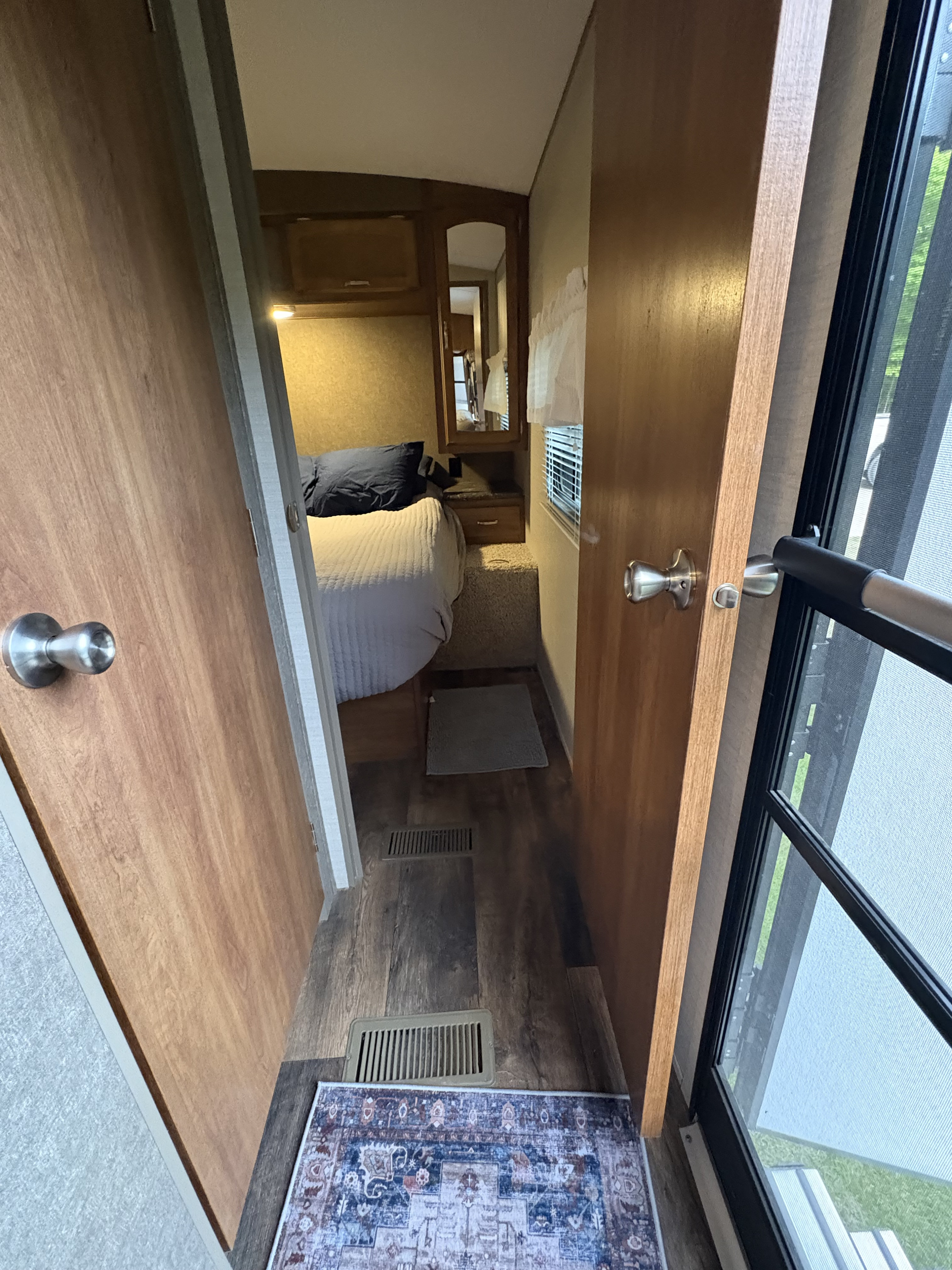 RV rental interior: A cozy hallway leads to a bedroom, with a patterned rug & an open door showing outside greenery.. Keystone RV Springdale 2016