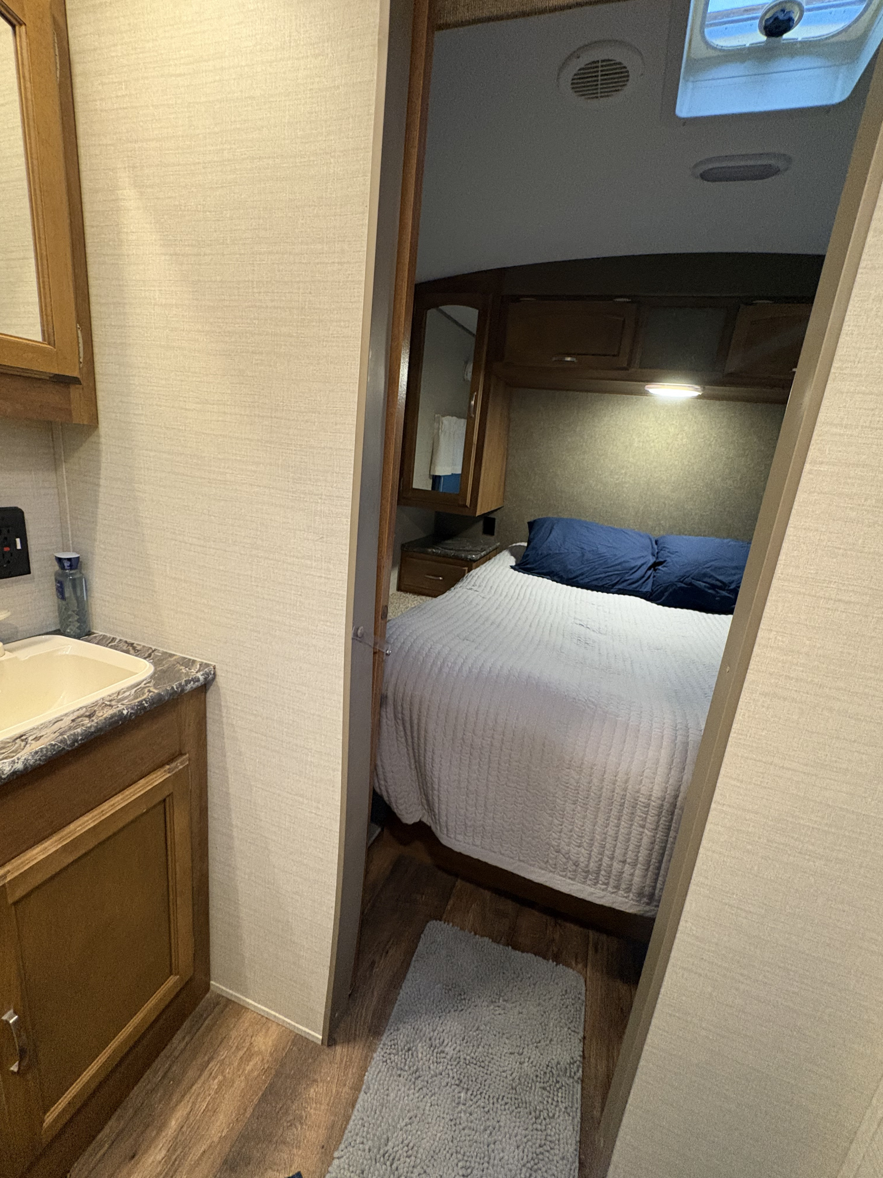 Inside an RV rental: a compact bedroom with a bed and blue pillows, viewed from a small bathroom vanity area with a sink.. Keystone RV Springdale 2016