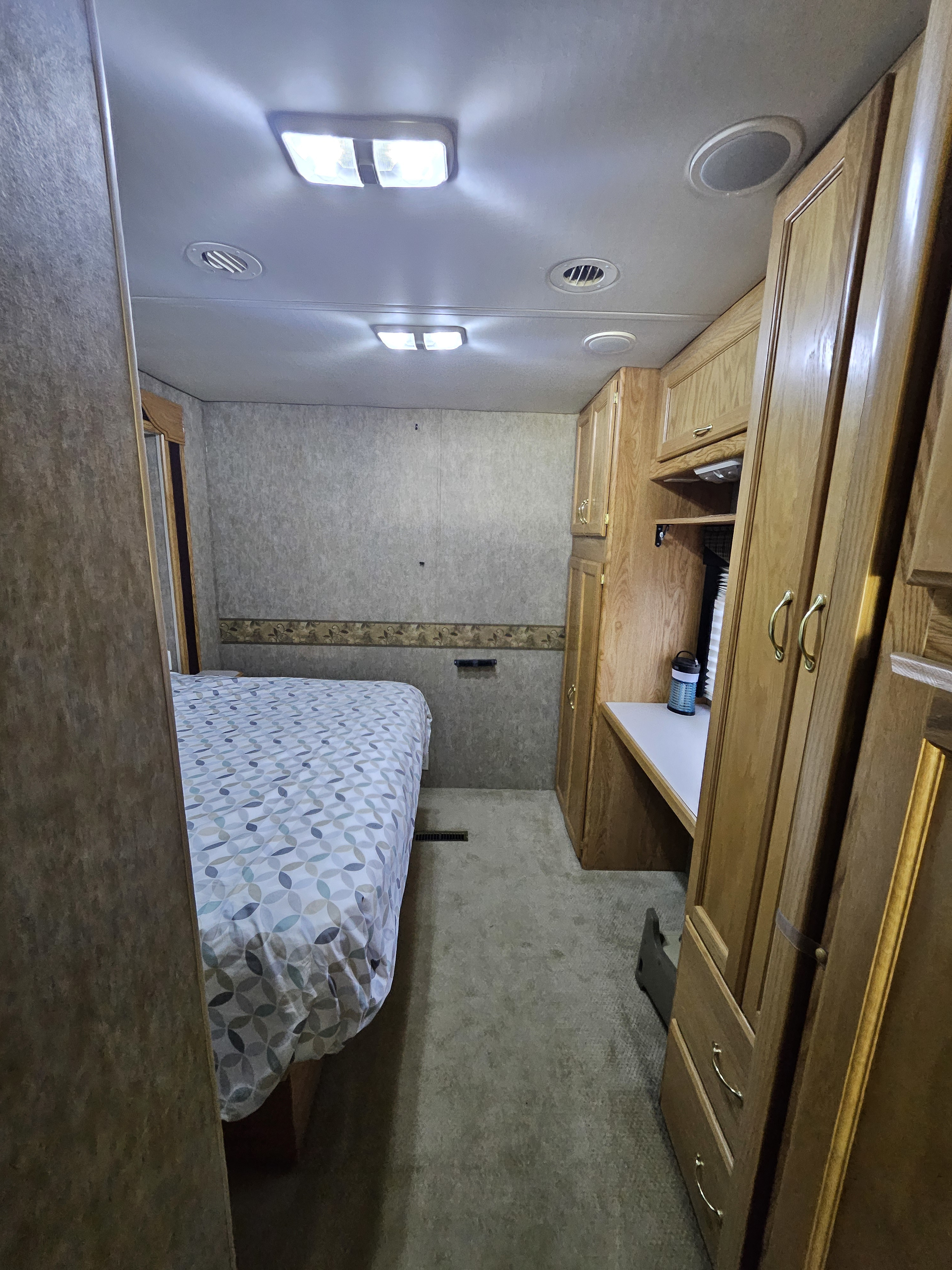 RV rental bedroom interior with a bed, wooden cabinets, and a desk, offering cozy accommodation.. Holiday Rambler Admiral SE 2006