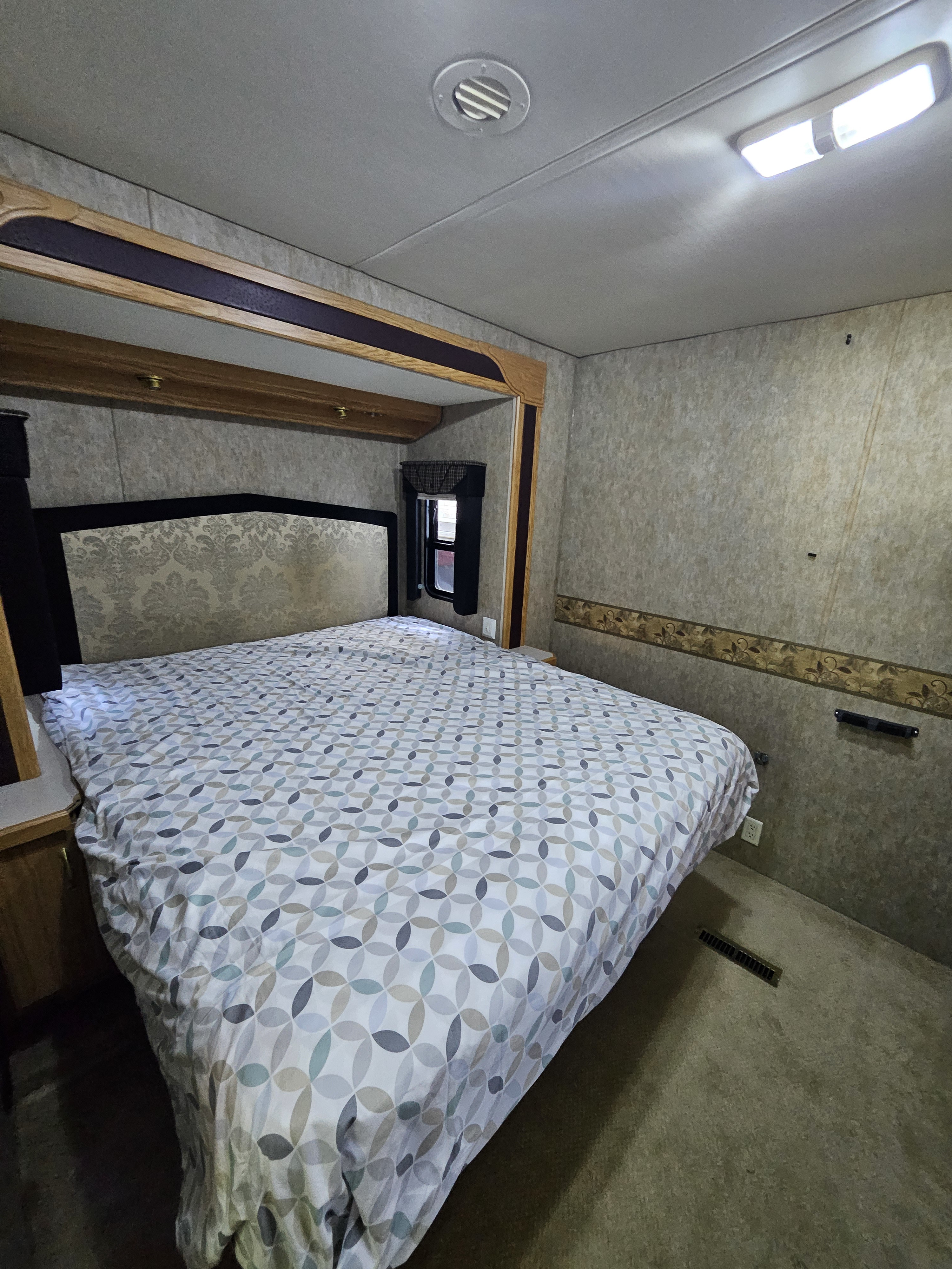 Experience comfort in this RV rental bedroom: a large bed with geometric comforter, window, and ceiling vent.. Holiday Rambler Admiral SE 2006
