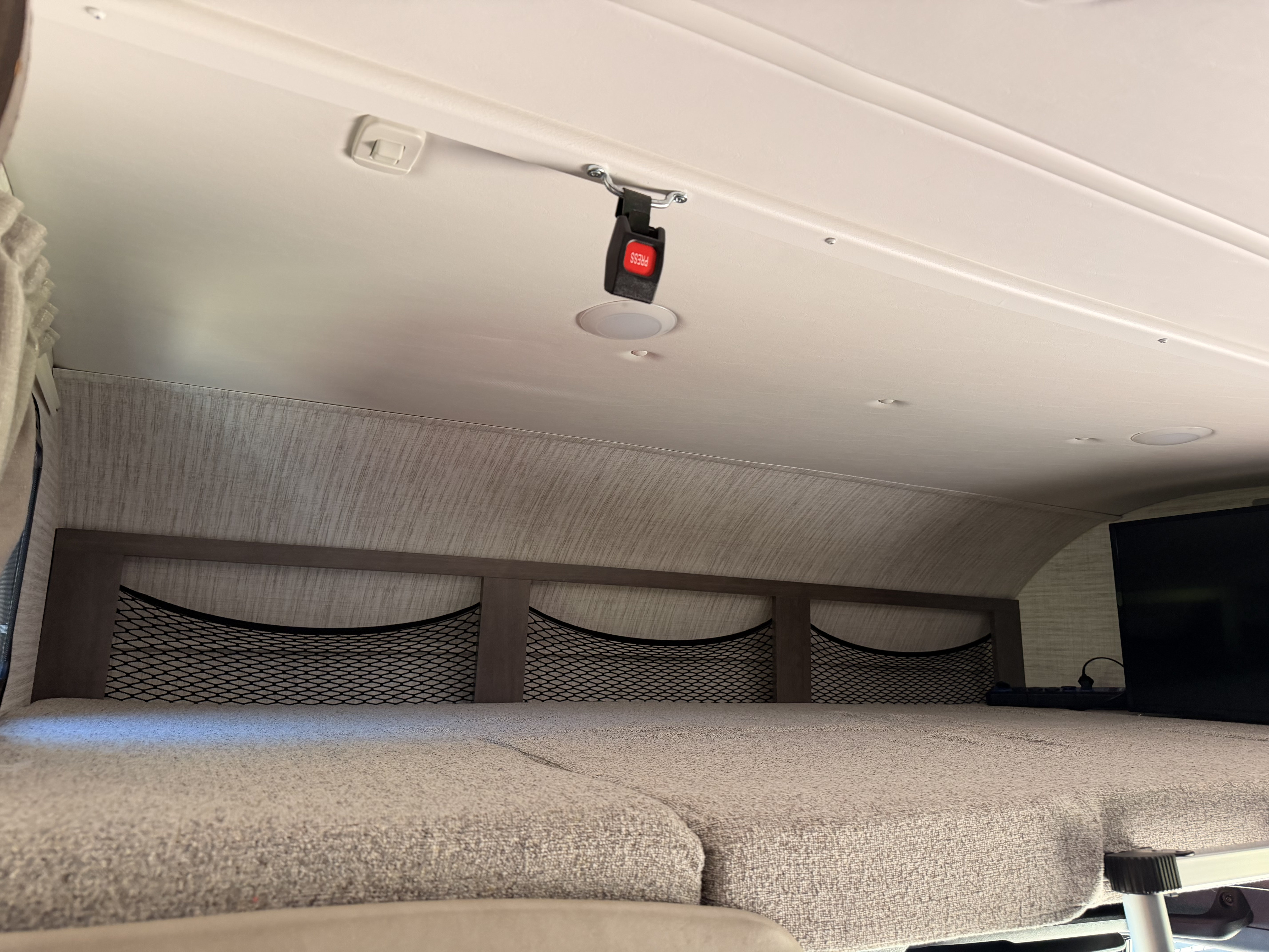 Interior of an RV rental, featuring an overhead bunk bed with a mattress, storage nets, ceiling lights, and a safety seatbelt buckle.. Jayco Melbourne 2024