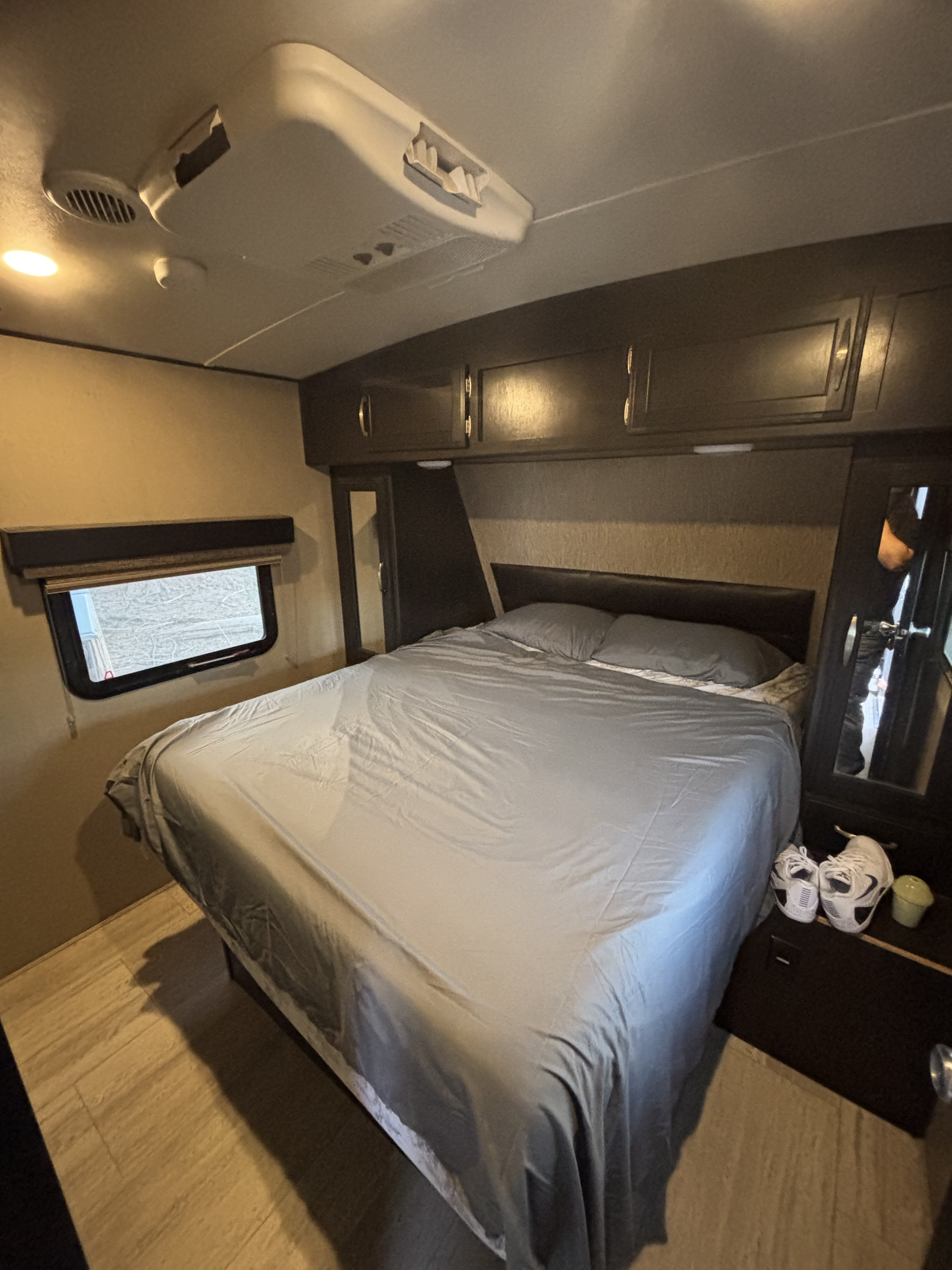 Cozy RV rental bedroom featuring a comfortable bed with gray sheets, overhead storage, a window, and a ceiling AC unit.. Grand Design Imagine 2018