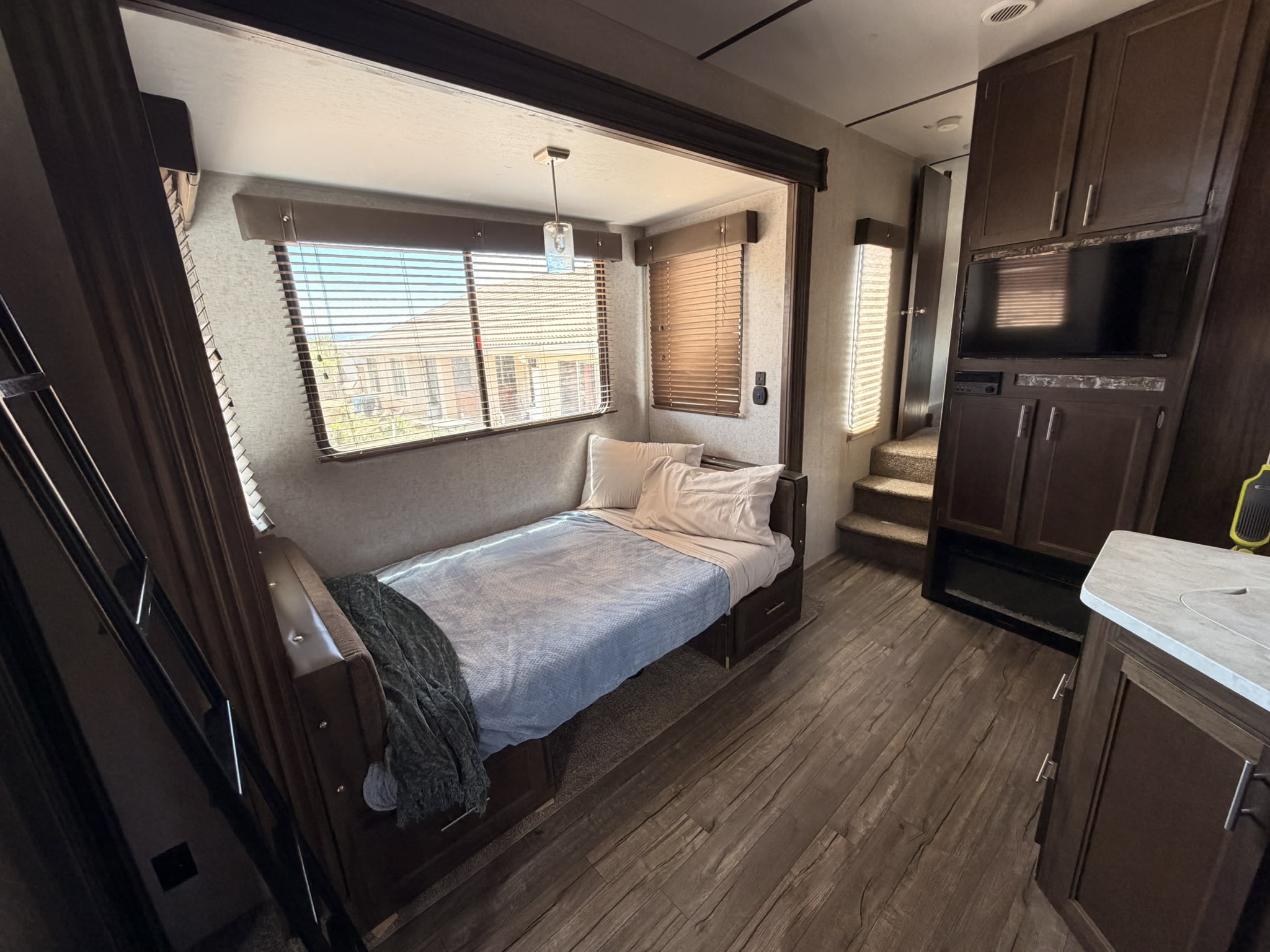 Cozy RV rental interior featuring a bedroom with a bed & windows, and a living area with a TV, cabinets, and stairs.. Forest River Cherokee Wolf Pack Toy Hauler 2018