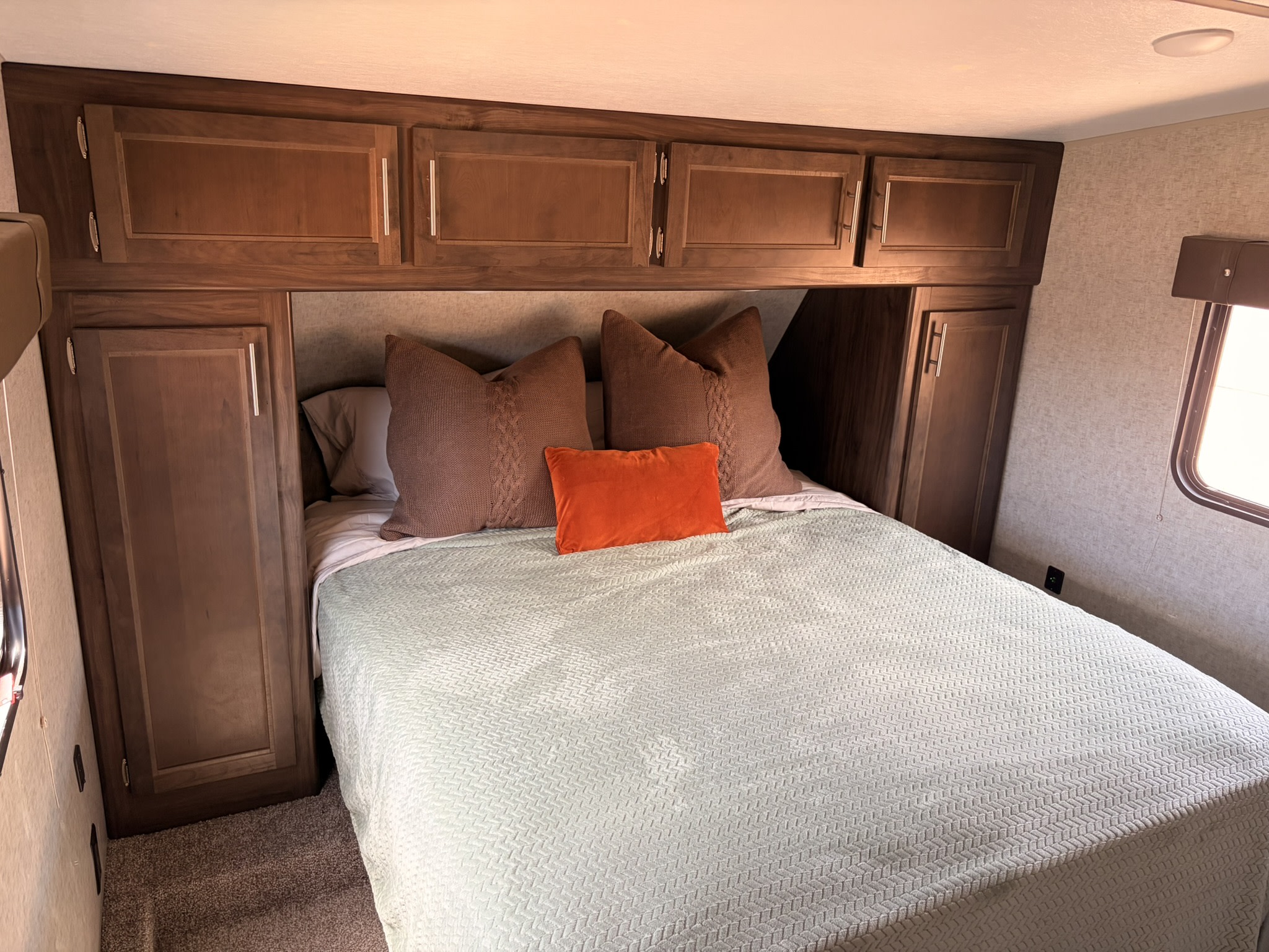 Cozy RV rental bedroom with a comfy bed, green blanket, brown pillows, and ample wooden overhead storage.. Forest River Cherokee Wolf Pack Toy Hauler 2018