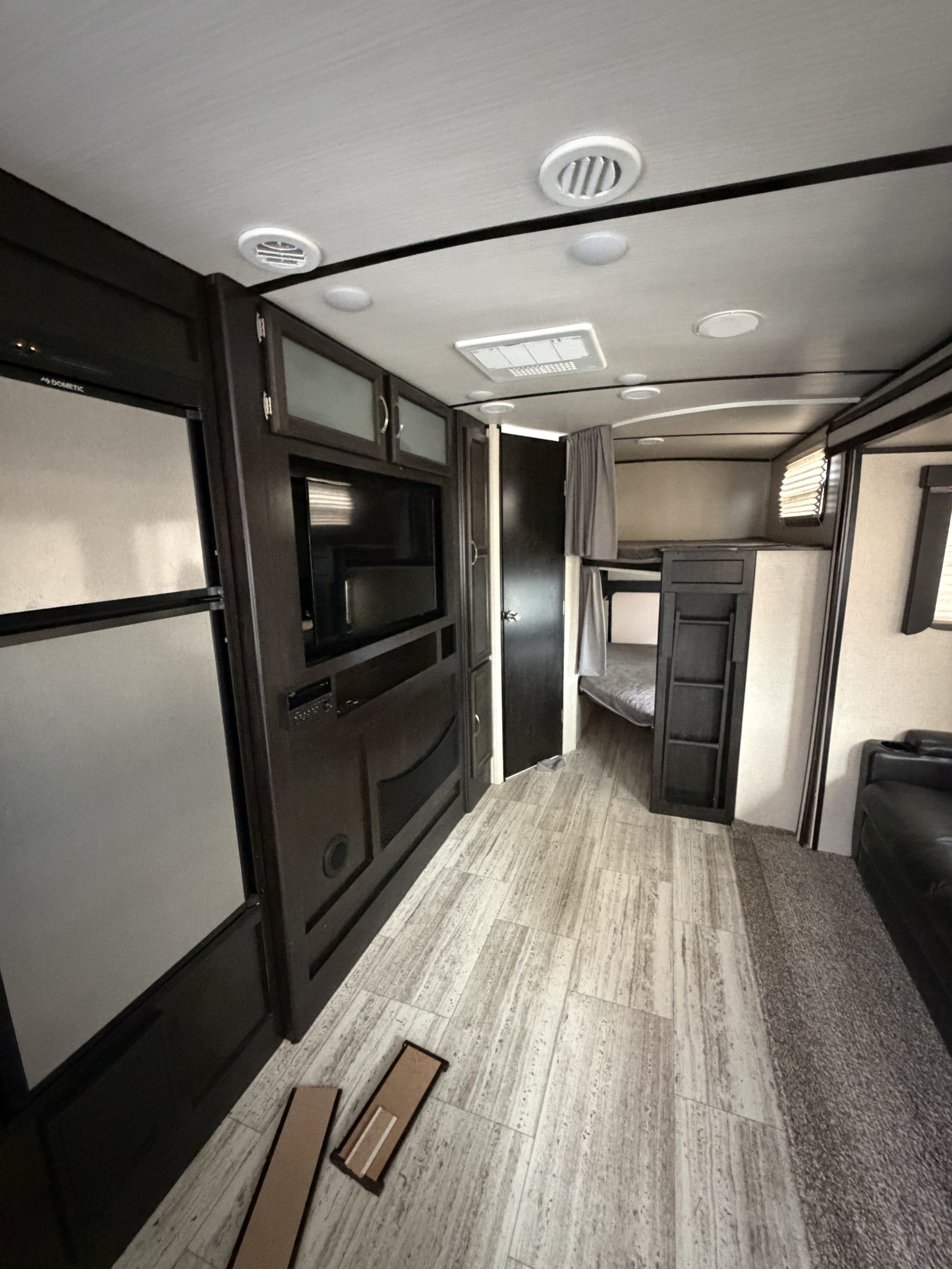 Modern RV rental interior showing dark cabinetry with TV, refrigerator, bunk beds, and light wood-look flooring.. Coachmen Spirit Lite Ultra 2963BH 2020