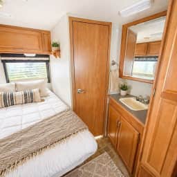 Inside a comfortable RV rental: A cozy bedroom with patterned blankets, wooden door, and glimpse of the kitchen/bath mirror.. Winnebago Aspect 2006