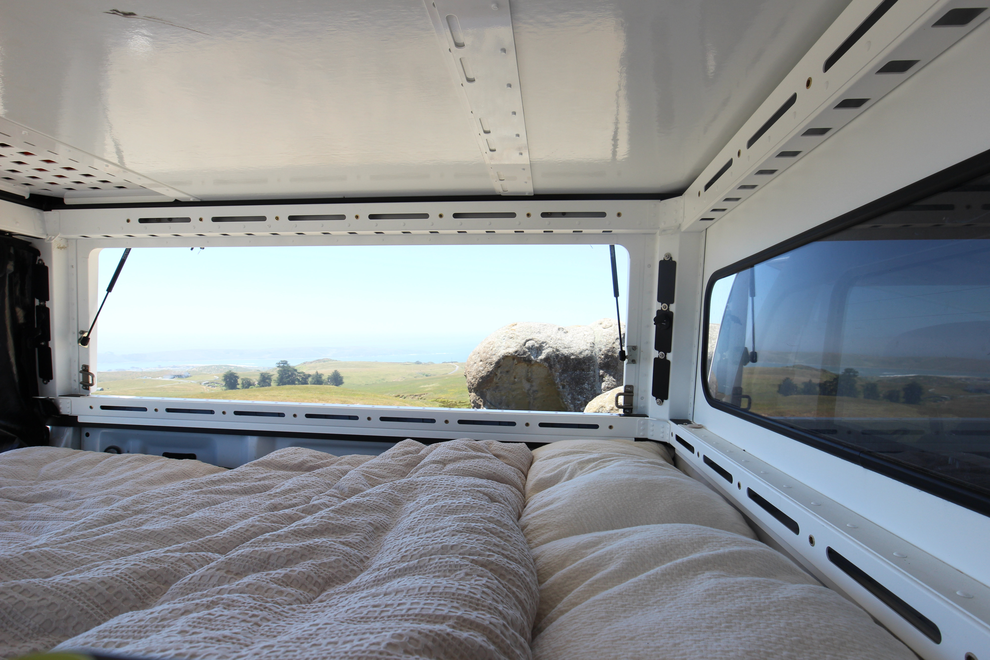 Cozy bed inside an RV rental offering scenic views of coastal hills & ocean. Ideal for camping adventures!. Ford Ford F150 2017