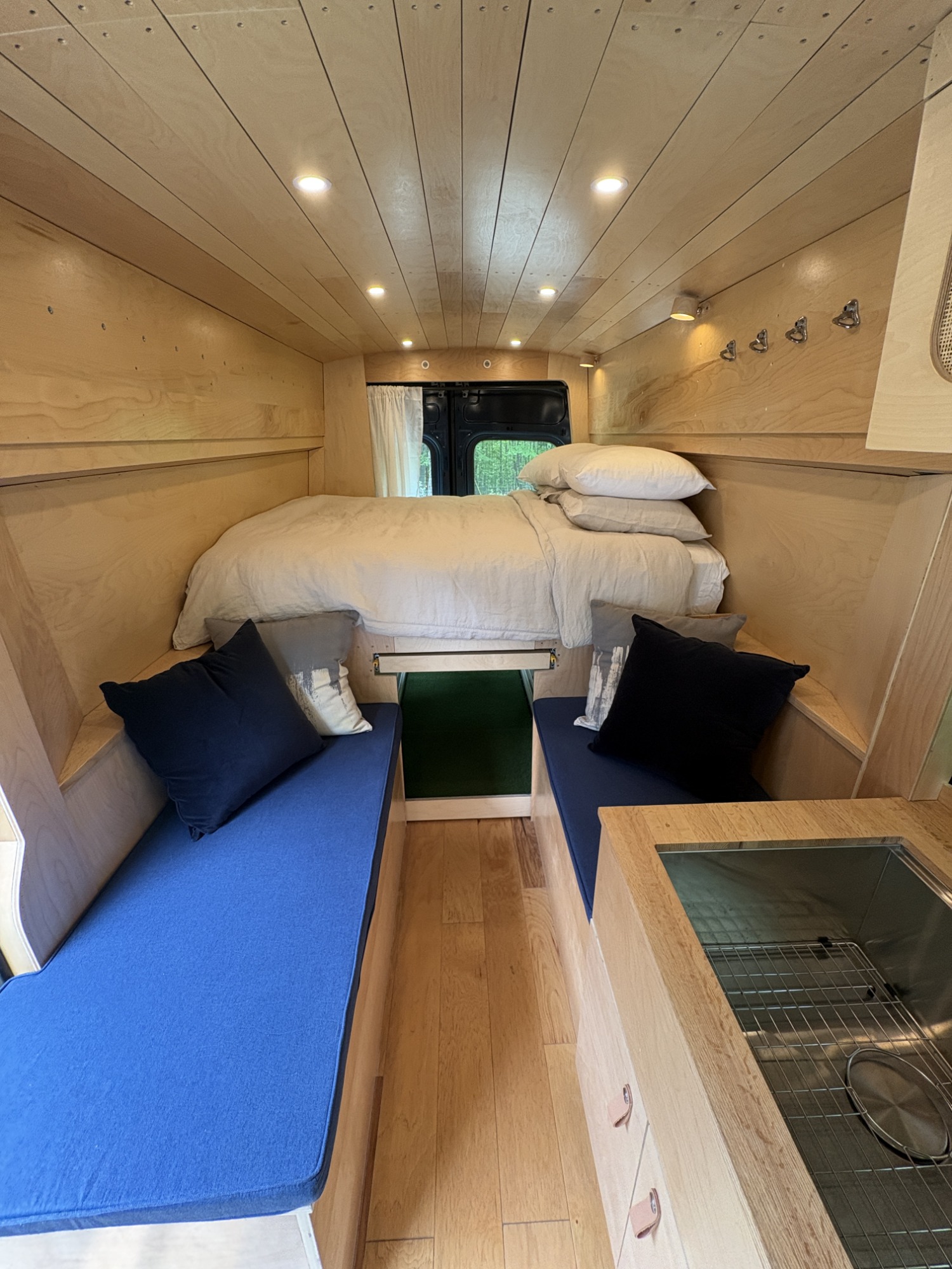 Step inside this cozy RV rental with natural wood walls, a comfy bed, blue cushions, and a functional kitchen sink.. Ford Transit custom 2020