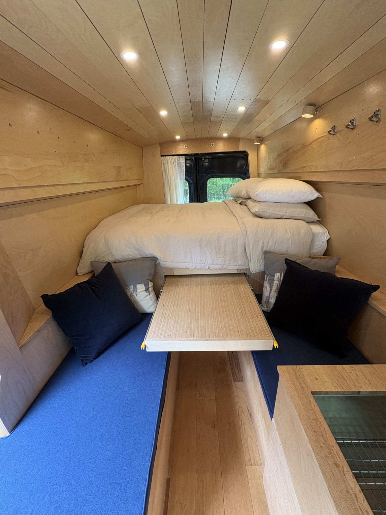 Cozy RV rental interior: wood-paneled walls, bed, dining area with blue cushions. Ideal for travel.. Ford Transit custom 2020