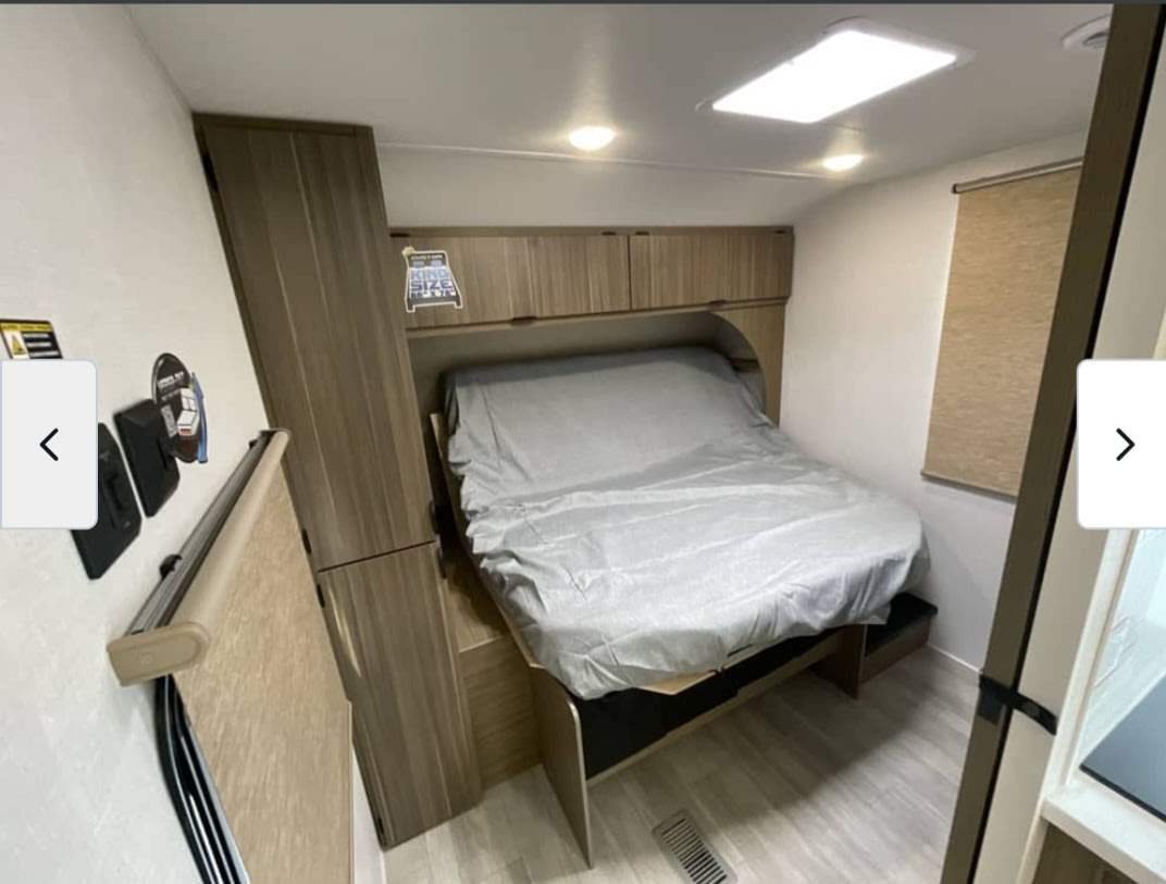 This RV rental bedroom features a cozy bed with overhead cabinets and a window with a shade, offering compact comfort for your journey.. Forest River Salem 2026