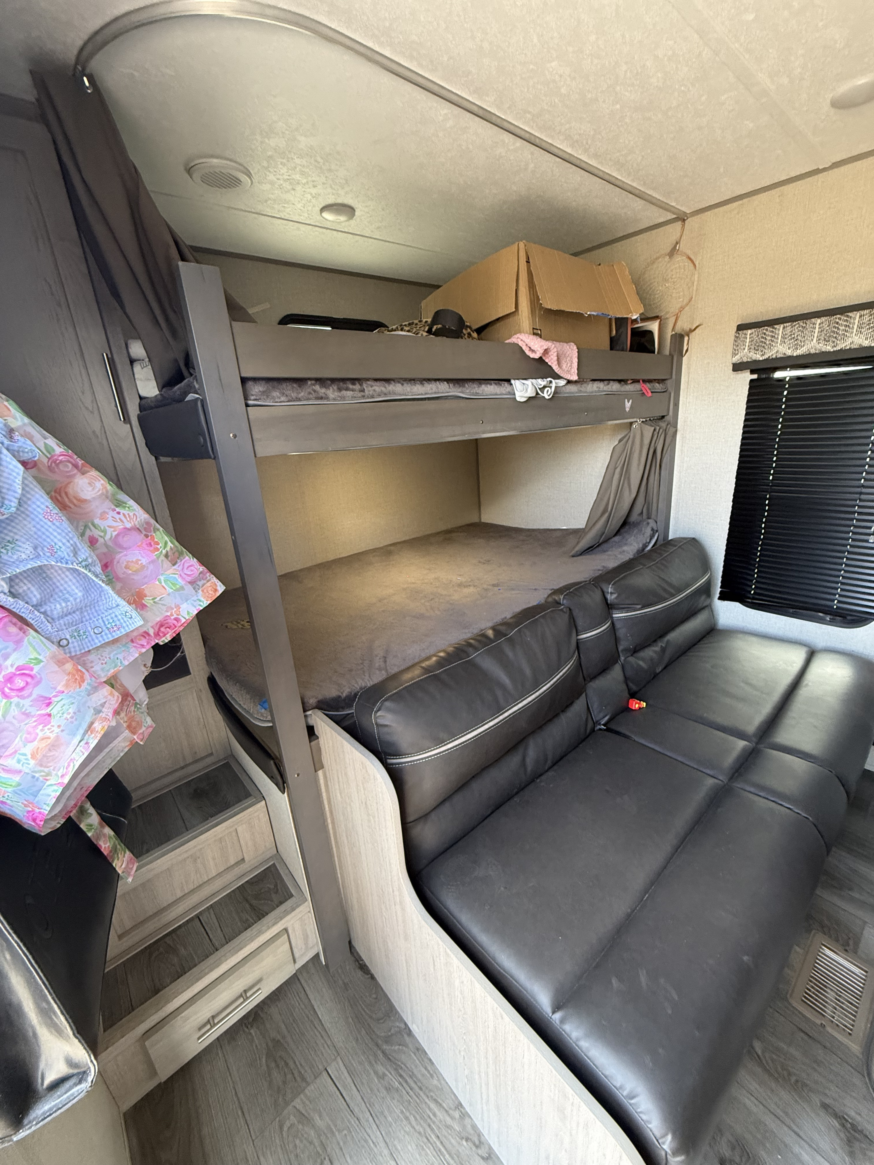 RV rental interior: stacked bunk beds, dark leather sofa, and built-in steps with storage. A compact living and sleeping area.. Coachmen Catalina summit series 2023