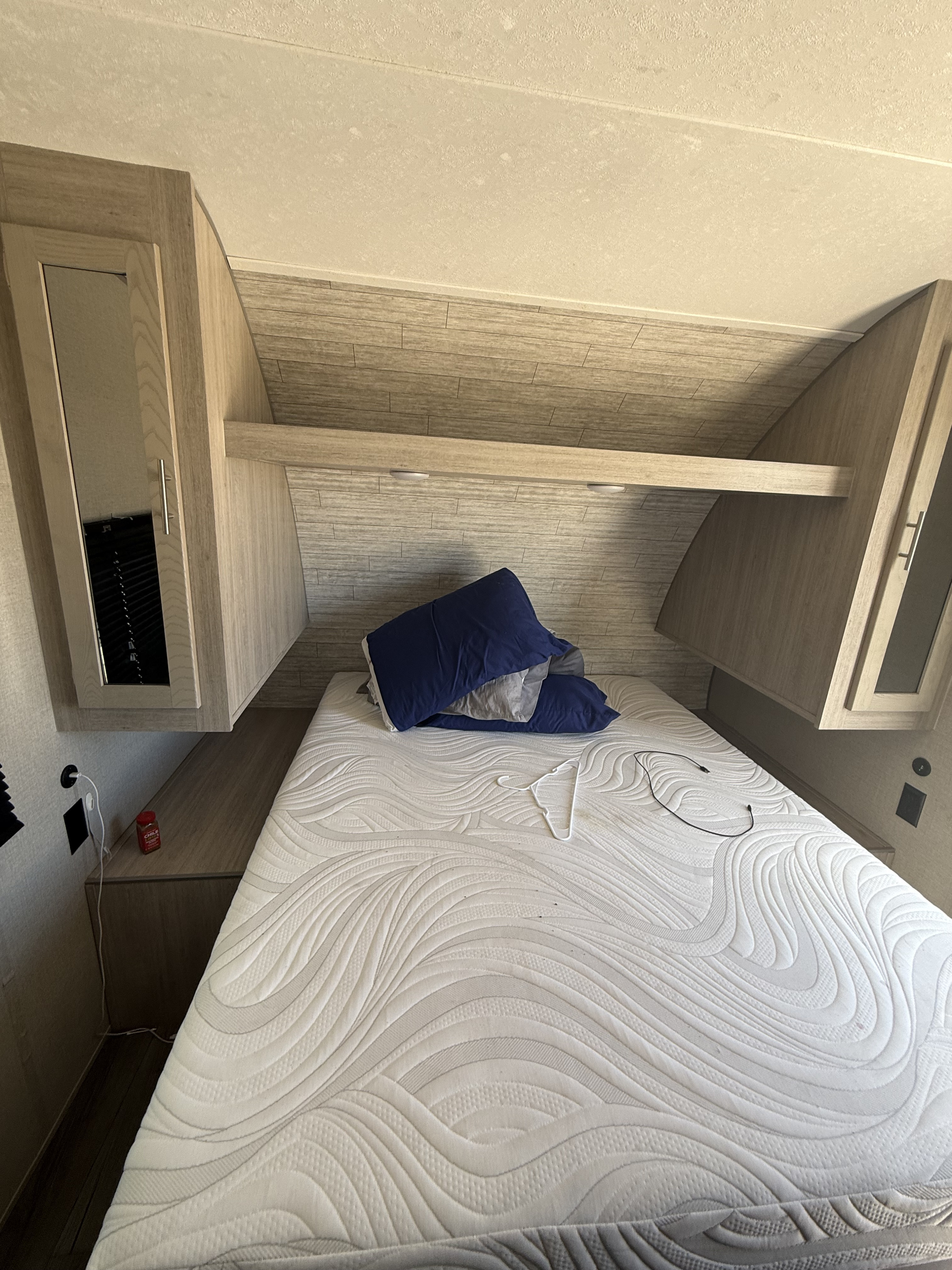 RV rental bedroom: interior with a quilted mattress, blue pillows, light wood cabinets, and shelving. A hanger and cable are on the bed.. Coachmen Catalina summit series 2023