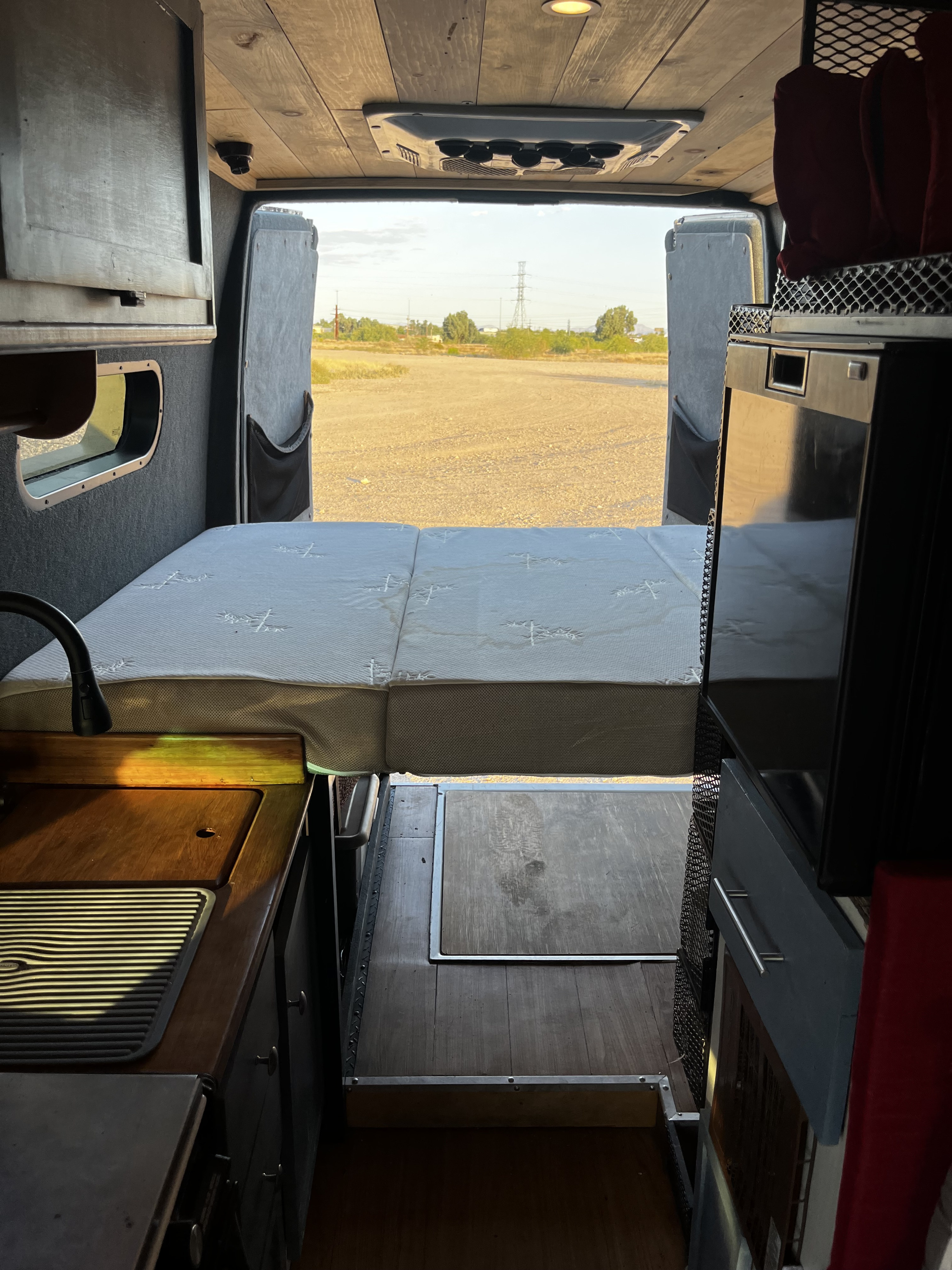 Inside a functional RV rental camper van: bed, kitchen area with sink, and open rear doors revealing a scenic outdoor view.. Mercedes Sprinter 2500 2002
