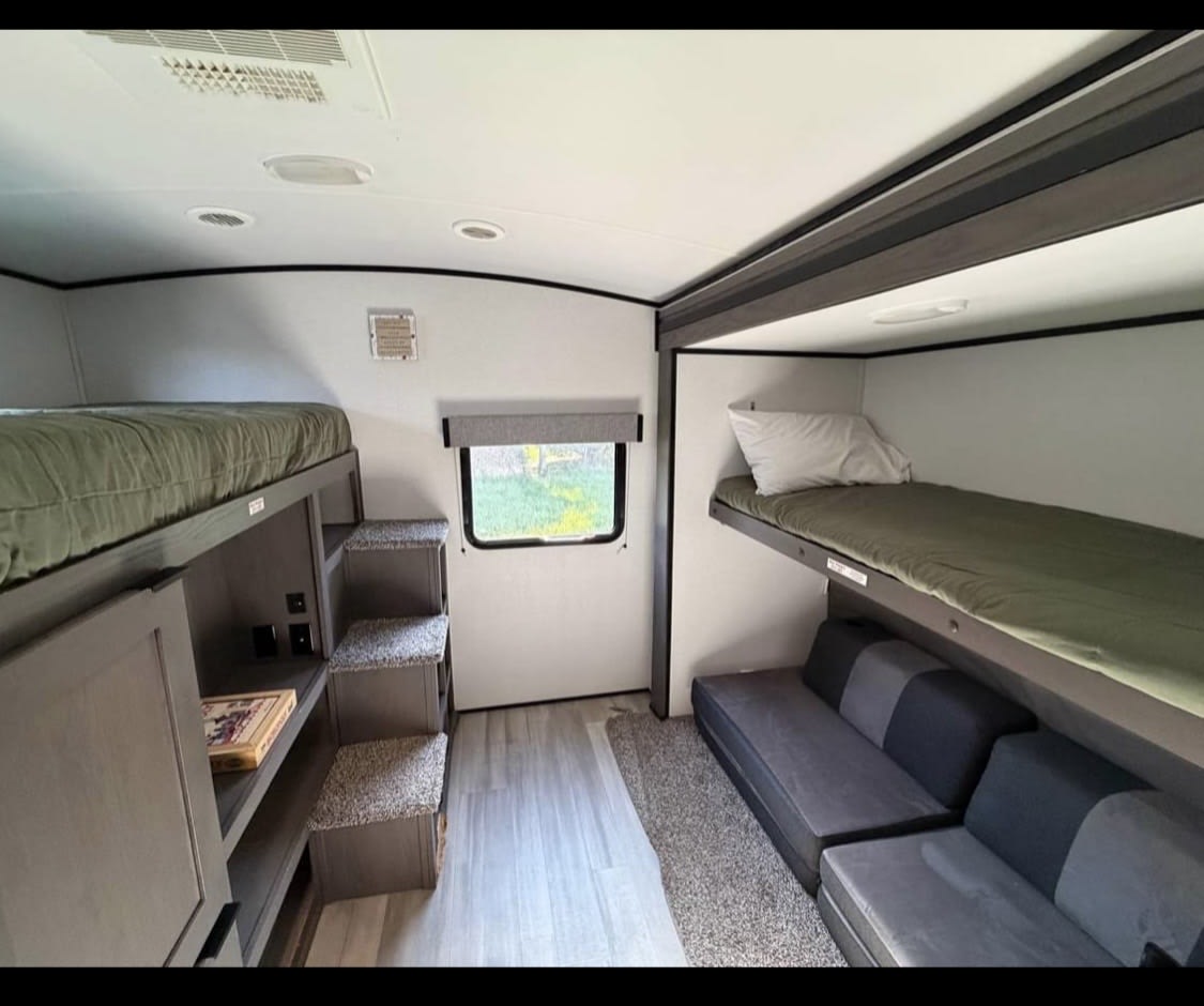 An RV rental bunkroom with olive green bunk beds, a comfortable gray sofa, and integrated storage steps for access.. Cruiser RV MPG Ultra Lite 2021