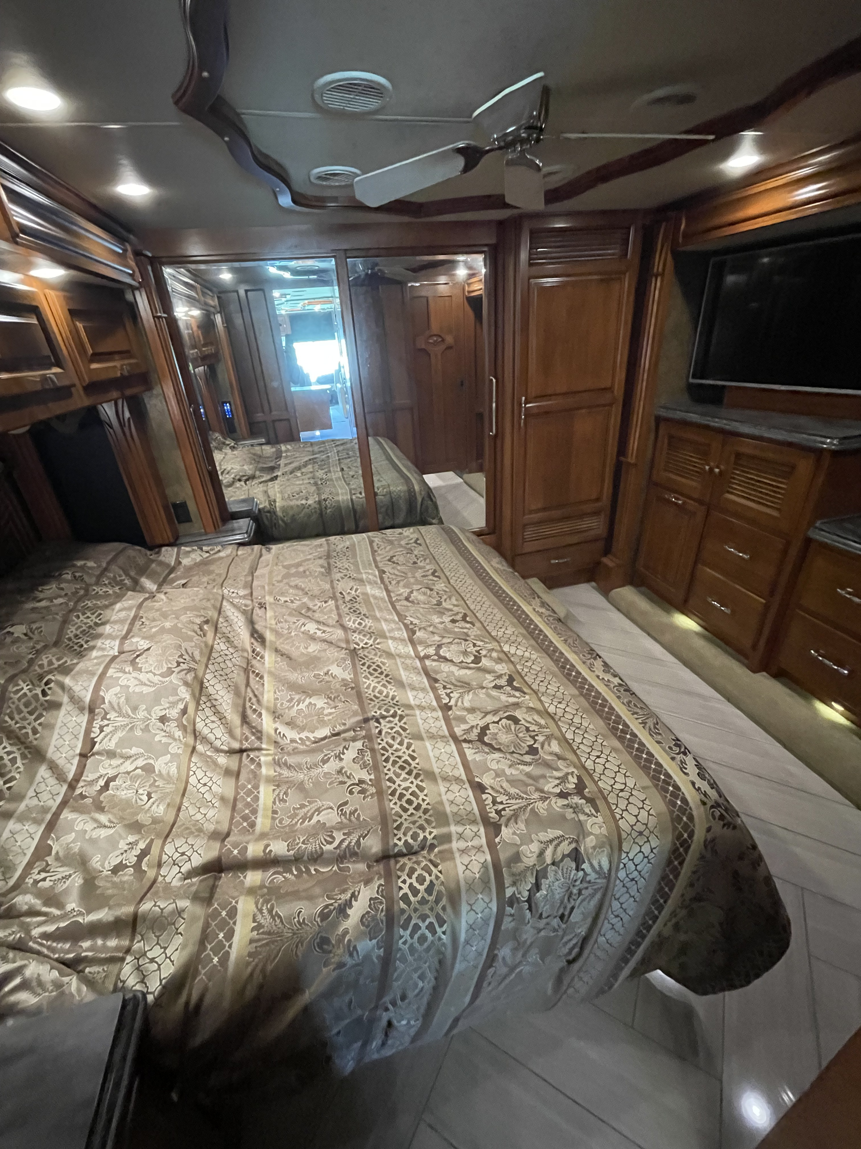 Spacious RV rental bedroom featuring a comfy patterned bed, wooden cabinetry, mounted TV, and a ceiling fan.. Allegro Allegro Bus 2015