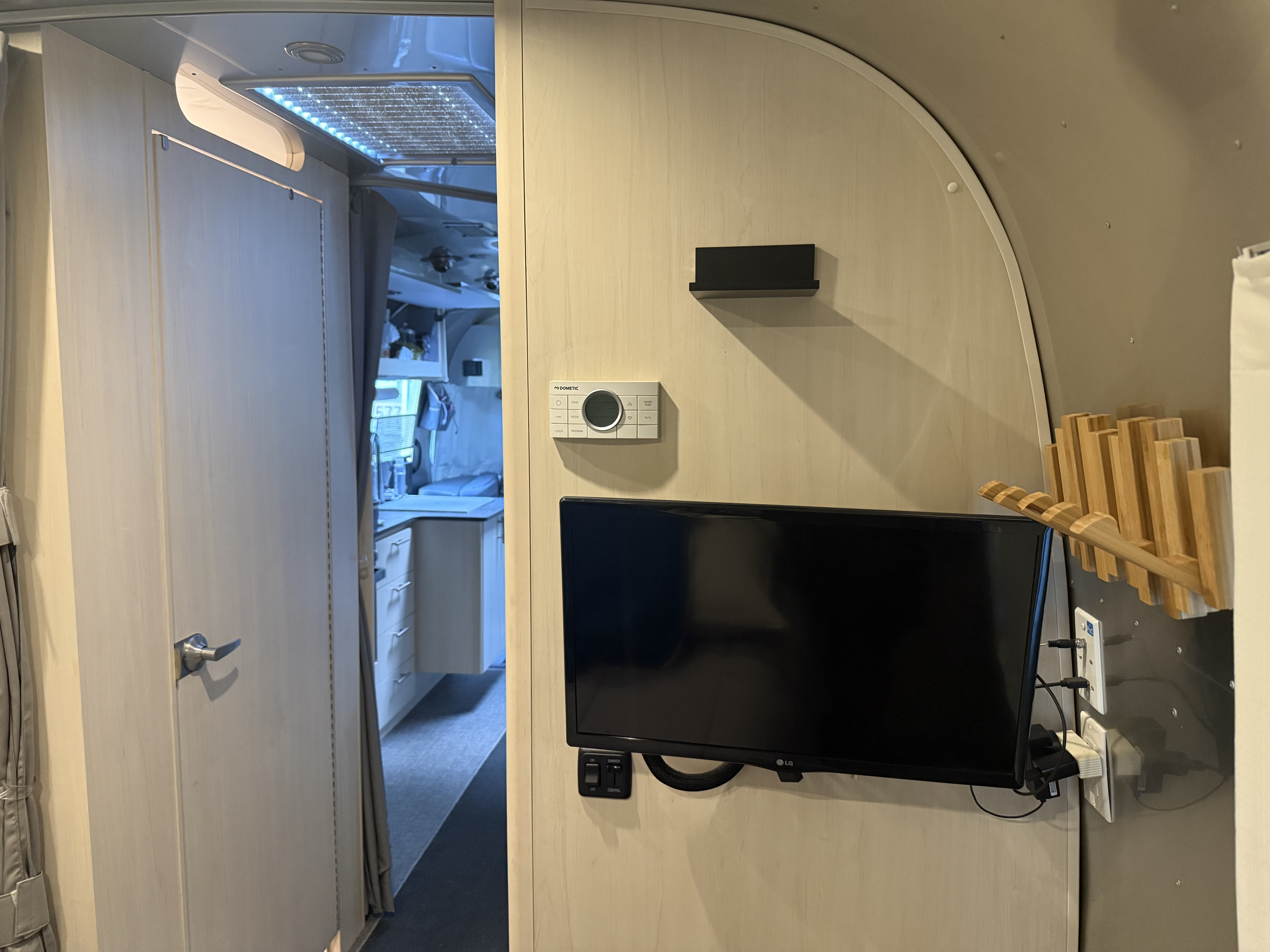 Interior of an rv rental showing a mounted TV, Dometic thermostat, and wooden rack, with a doorway to the kitchen/bathroom.. Airstream Flying Cloud 2021
