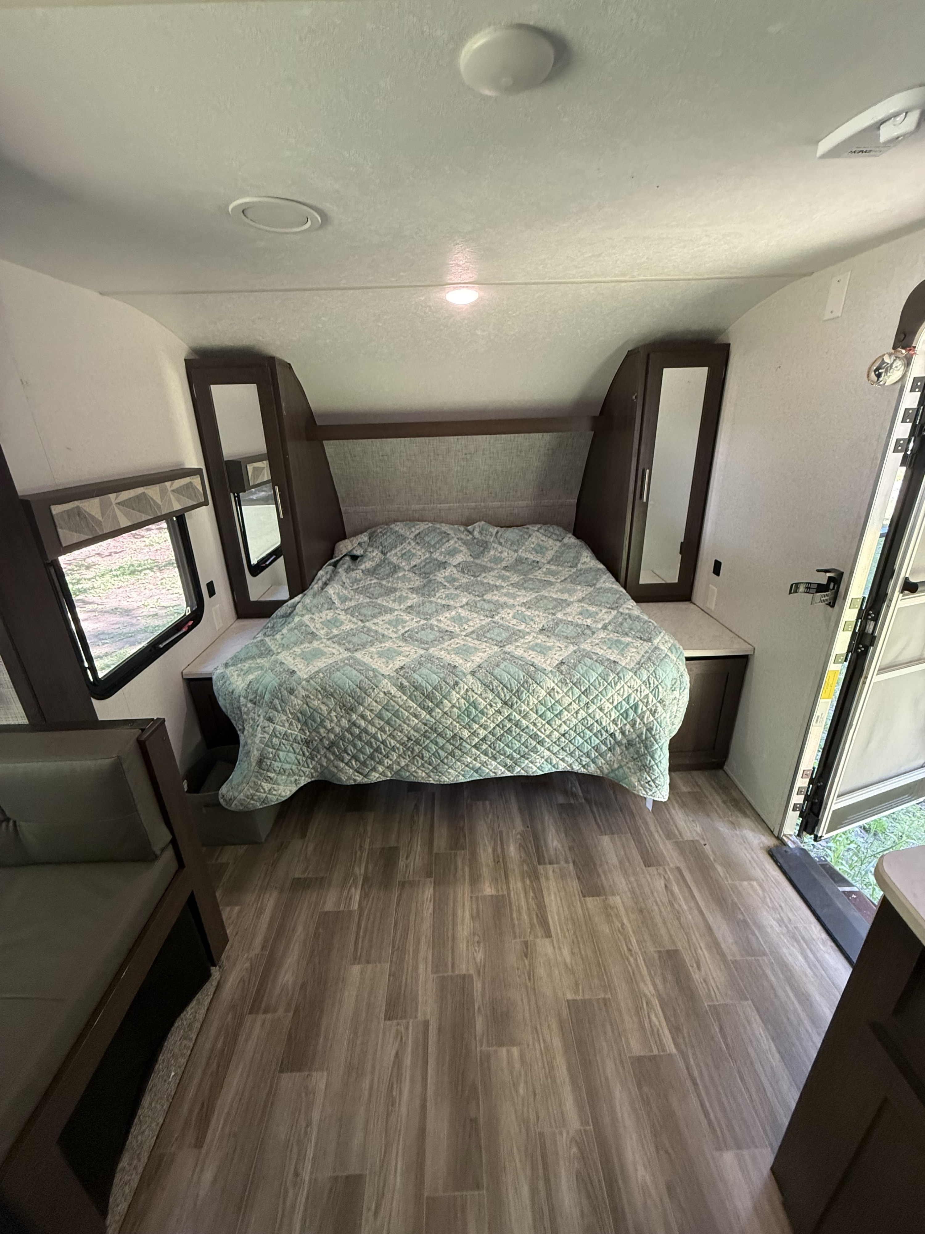 Cozy RV rental bedroom with a patterned quilt, dark wood accents, and laminate flooring, offering comfort and style.. Forest River Wildwood X-Lite 2019