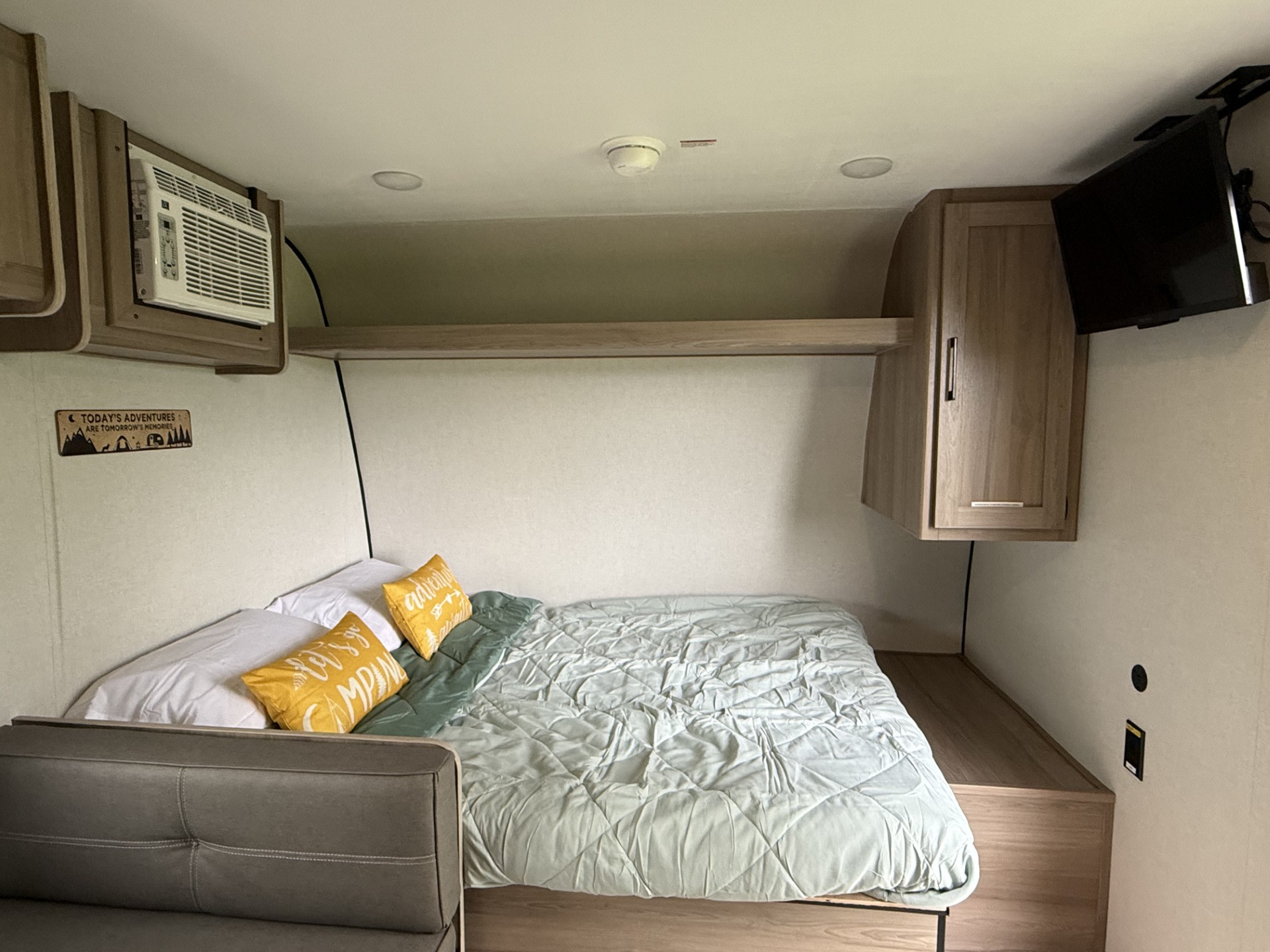 An RV rental bedroom features a bed with pillows, wall-mounted AC, TV, and overhead storage, perfect for travel comfort.. Keystone RV Coleman 2025