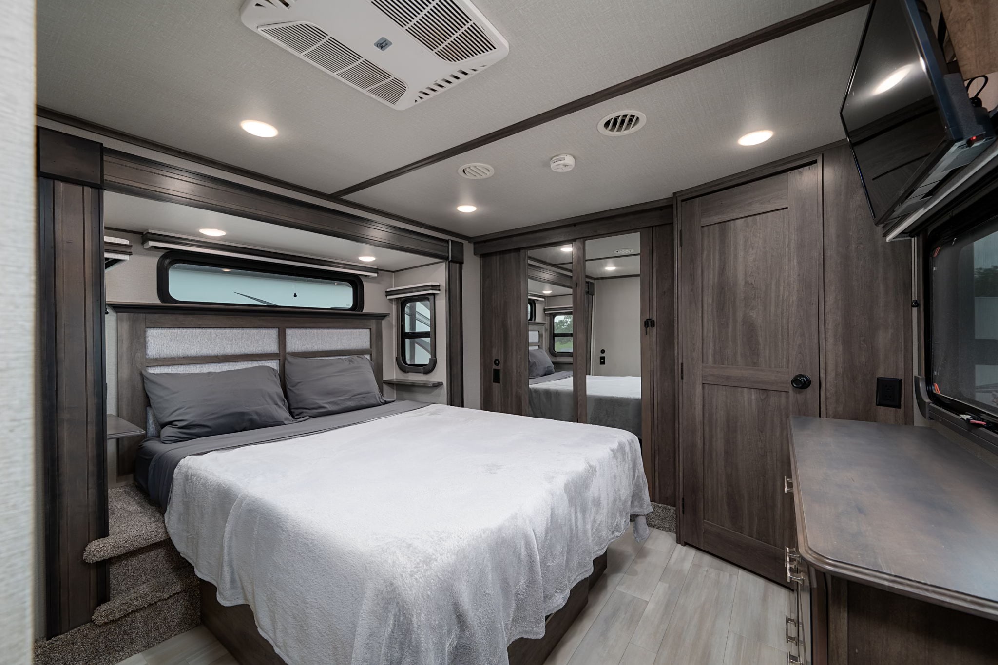 Step into this comfortable RV rental bedroom featuring a queen bed, storage, and modern design for your travels.. Grand Design Solitude 2022