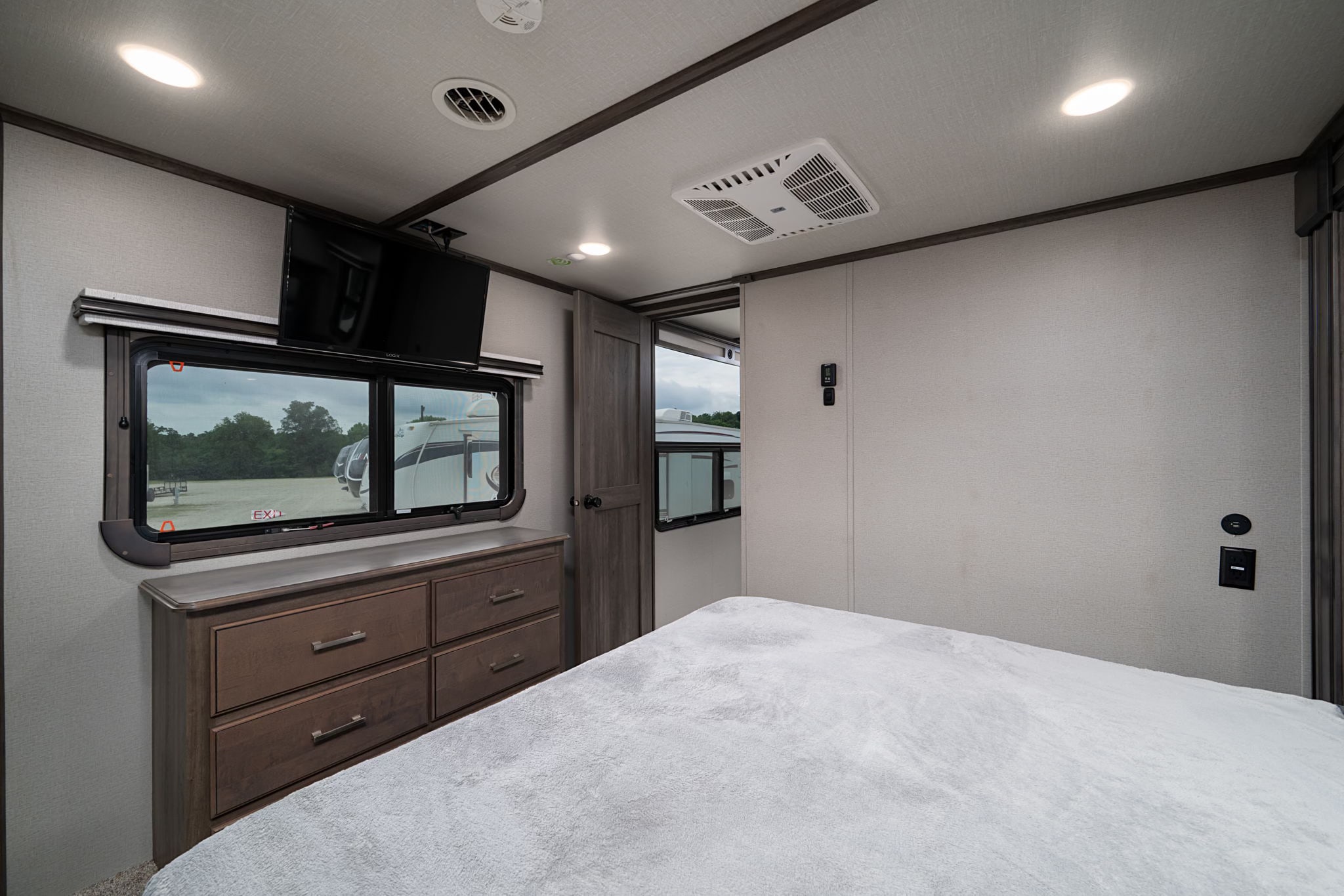 Comfortable rv rental bedroom with a mounted TV, dresser, and cozy bed for a relaxing journey.. Grand Design Solitude 2022