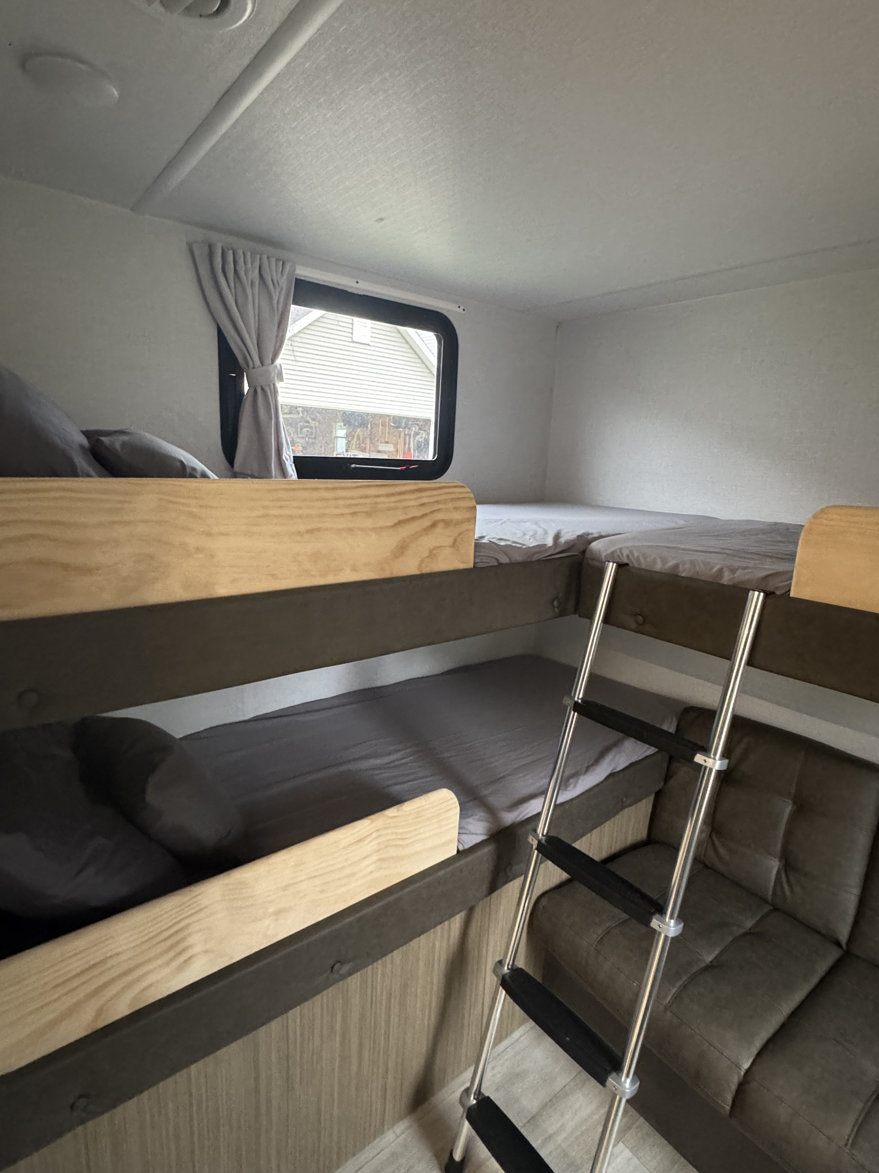 Inside an RV rental: built-in bunk beds with gray sheets, a climbing ladder, and a dark tufted sofa. Ready for travel!. Forest River X-Lite 2026