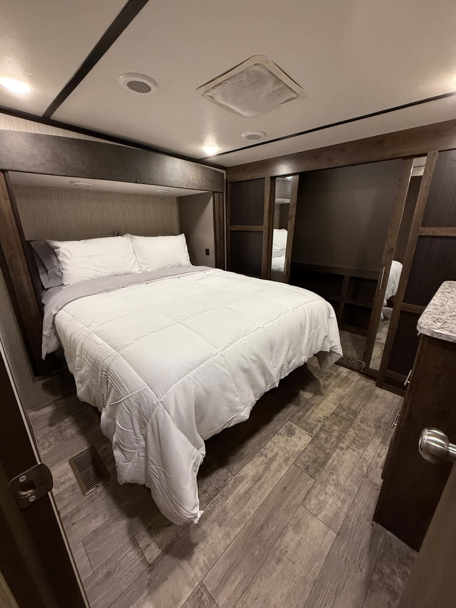 Cozy RV rental bedroom featuring a large bed with white bedding, dark wood accents, and light plank flooring.. Crossroads RV Volante 2020