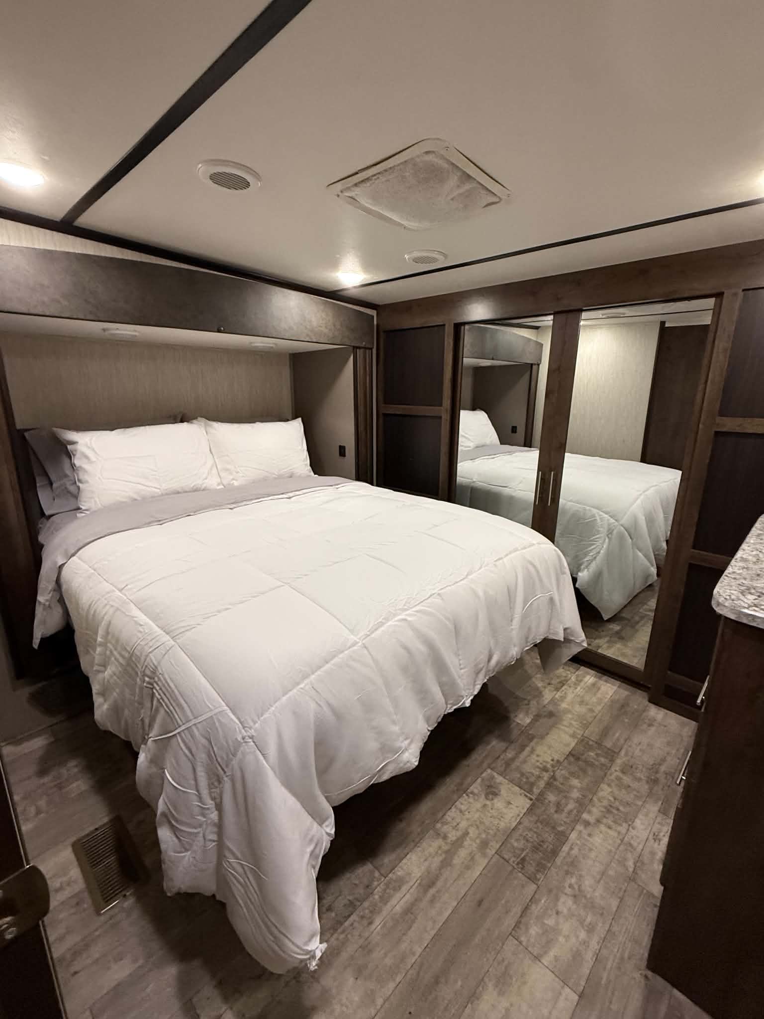 Inside an RV rental, this cozy bedroom offers a comfortable bed with white bedding, mirrored closet, and wood-look floor.. Crossroads RV Volante 2020