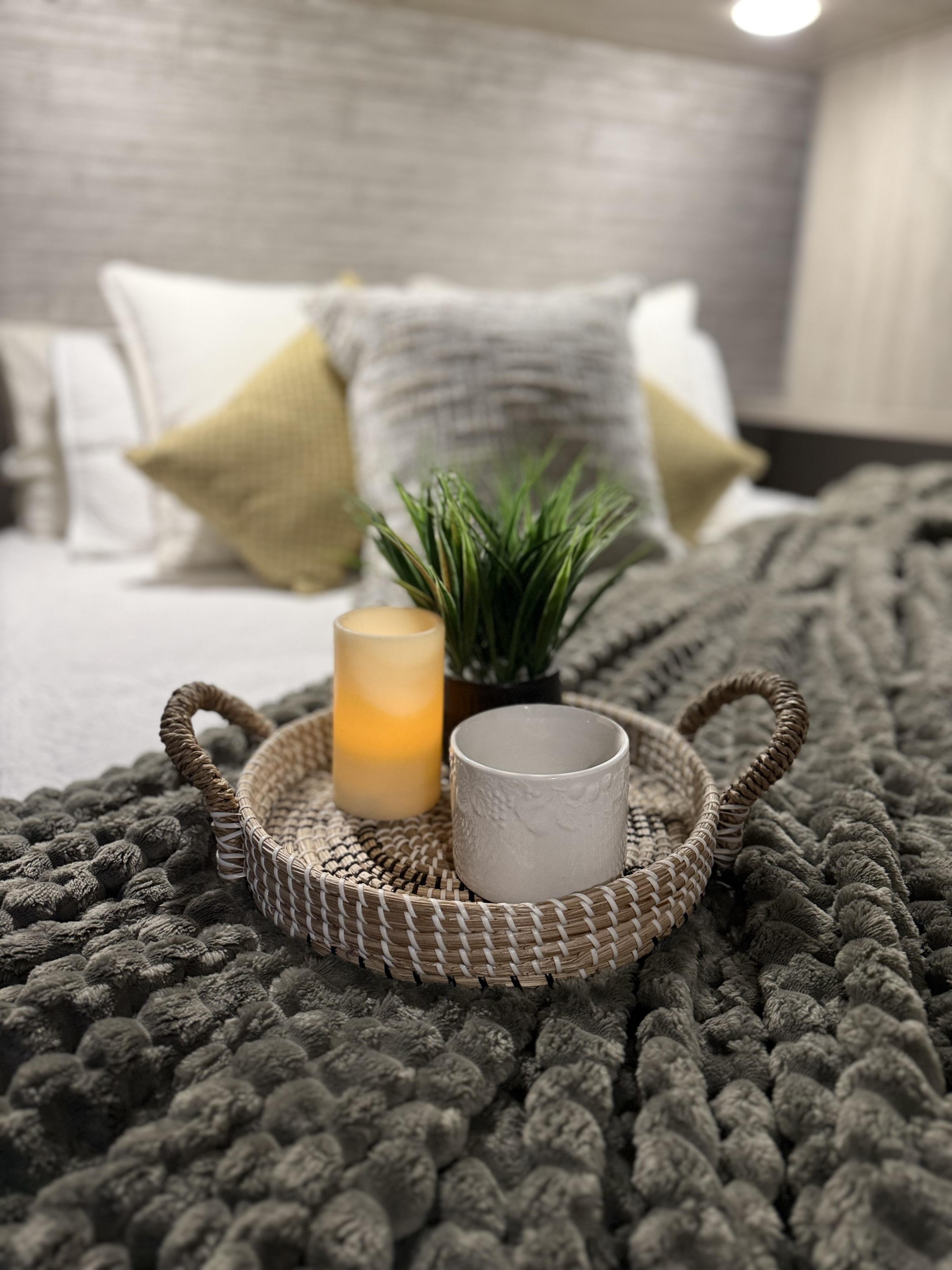 Cozy RV rental bedroom: woven tray with glowing candle, plant, mug on a plush gray blanket. Inviting decor.. Catalina 293TQBSCK 2026