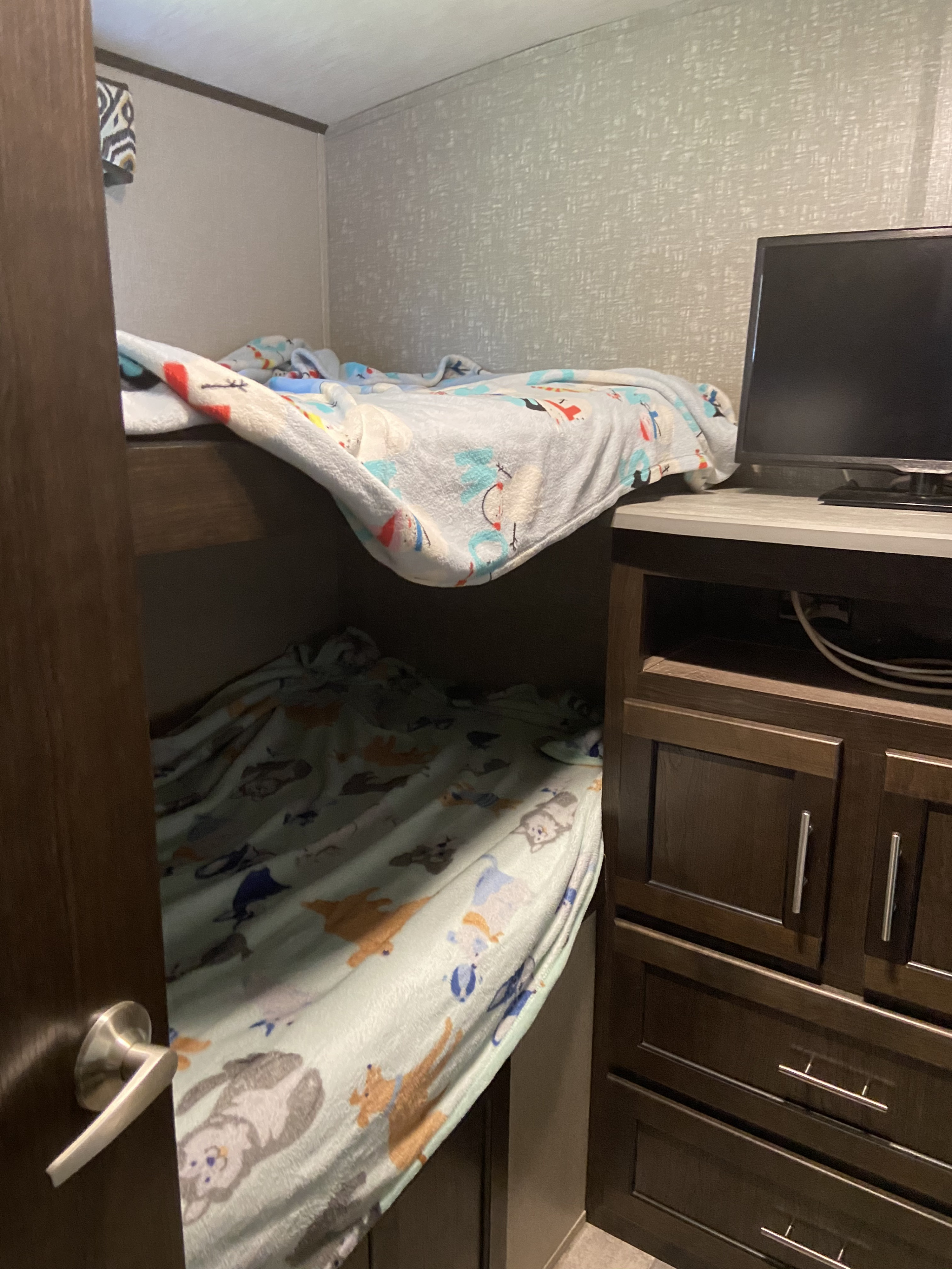 Inside an RV rental: bunk beds with patterned blankets and a TV on a dark wooden cabinet.. Cruiser RV Fun Finder Xtreme Lite 2017