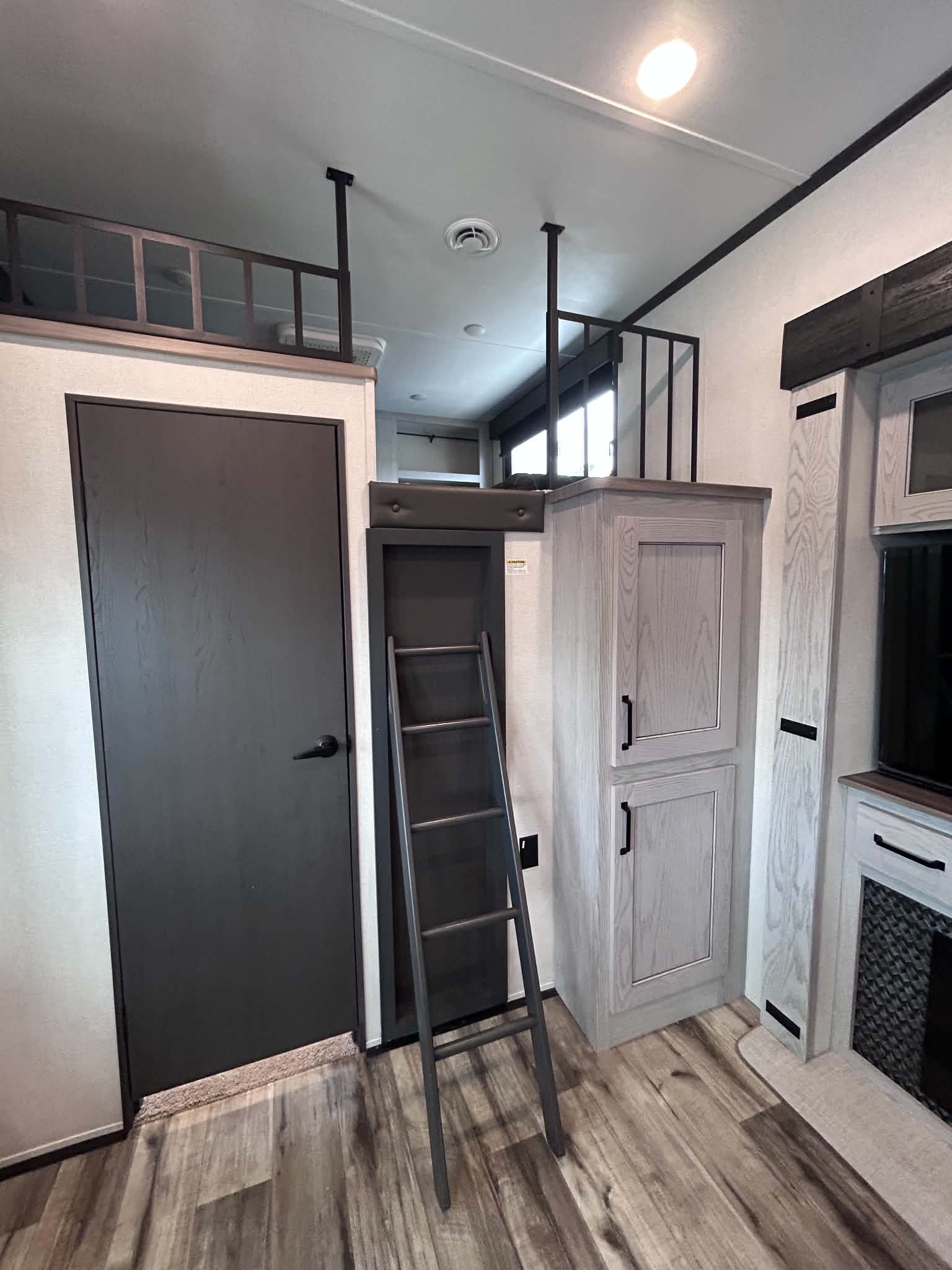 Spacious RV rental interior features a ladder to an upper loft/bunk, dark door, and light wood-look cabinets. Ideal for travel.. Keystone RV Montana High Country 2024