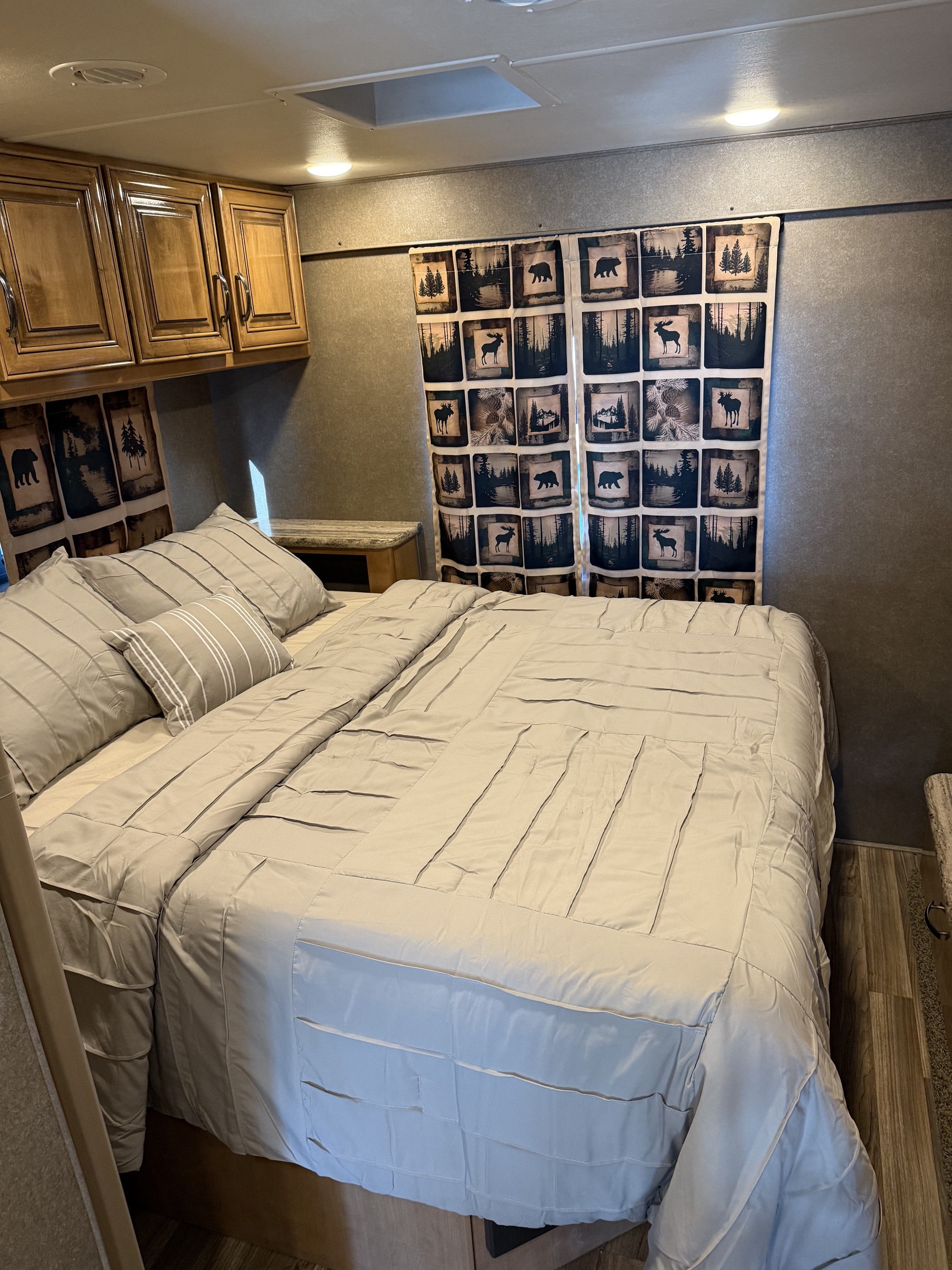 Cozy RV rental bedroom featuring a comfortable bed, wood cabinets, and nature-themed curtains, offering a rustic retreat.. Thor Quantum 2017