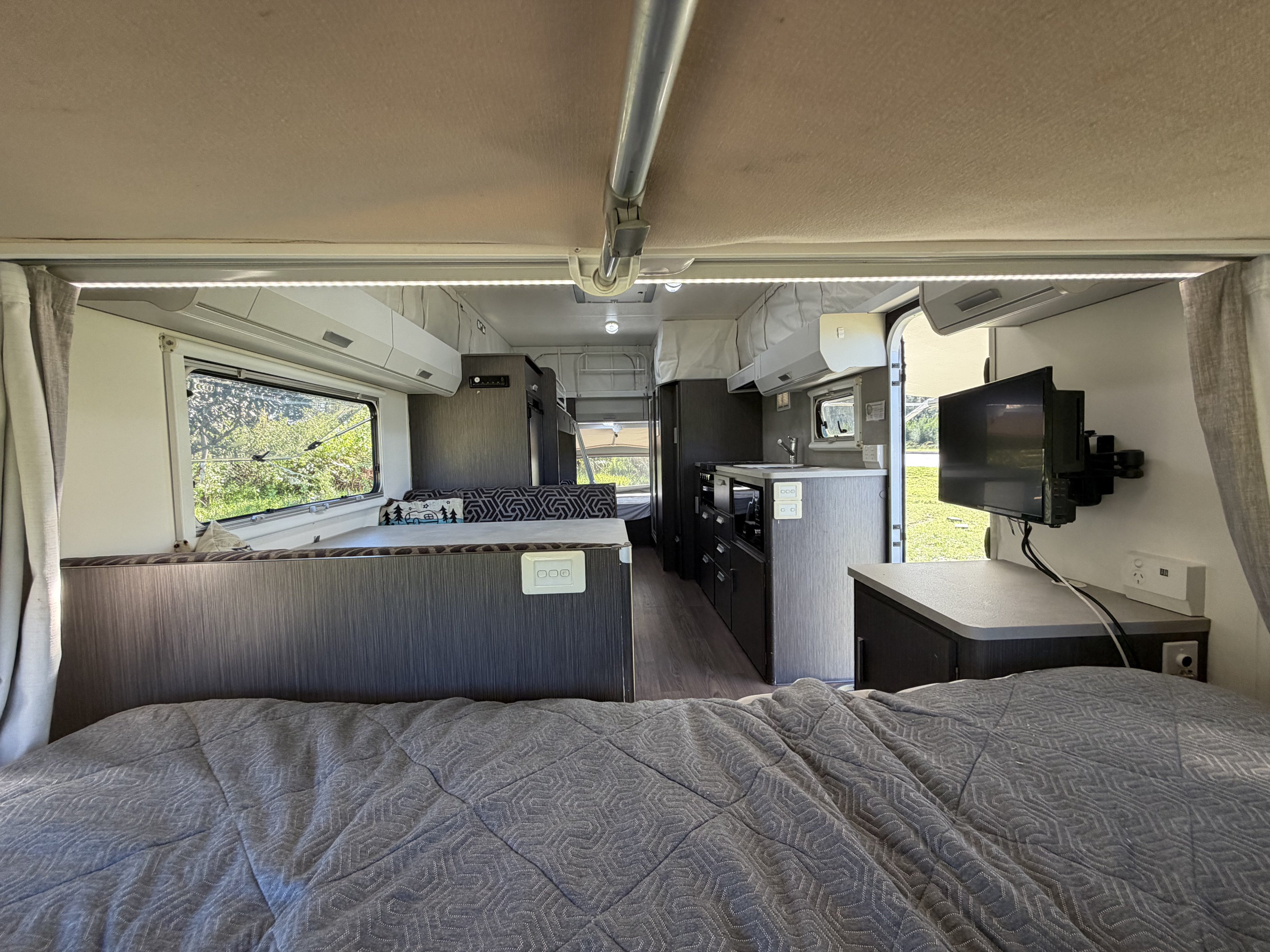 Comfortable rv rental interior from the bed, featuring kitchen, dining, and TV with a view of greenery outside.. Expanda Outback 2018