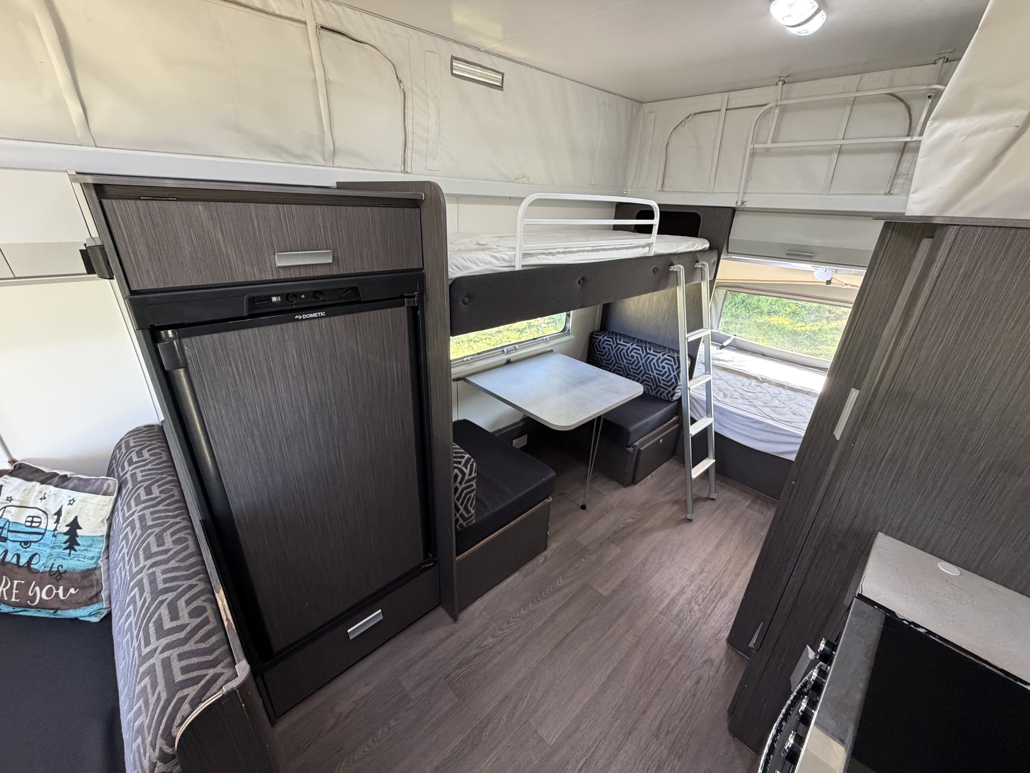 Inside a cozy RV rental: bunk beds with ladder, dinette, fridge, and pop-up sections for family adventures.. Expanda Outback 2018