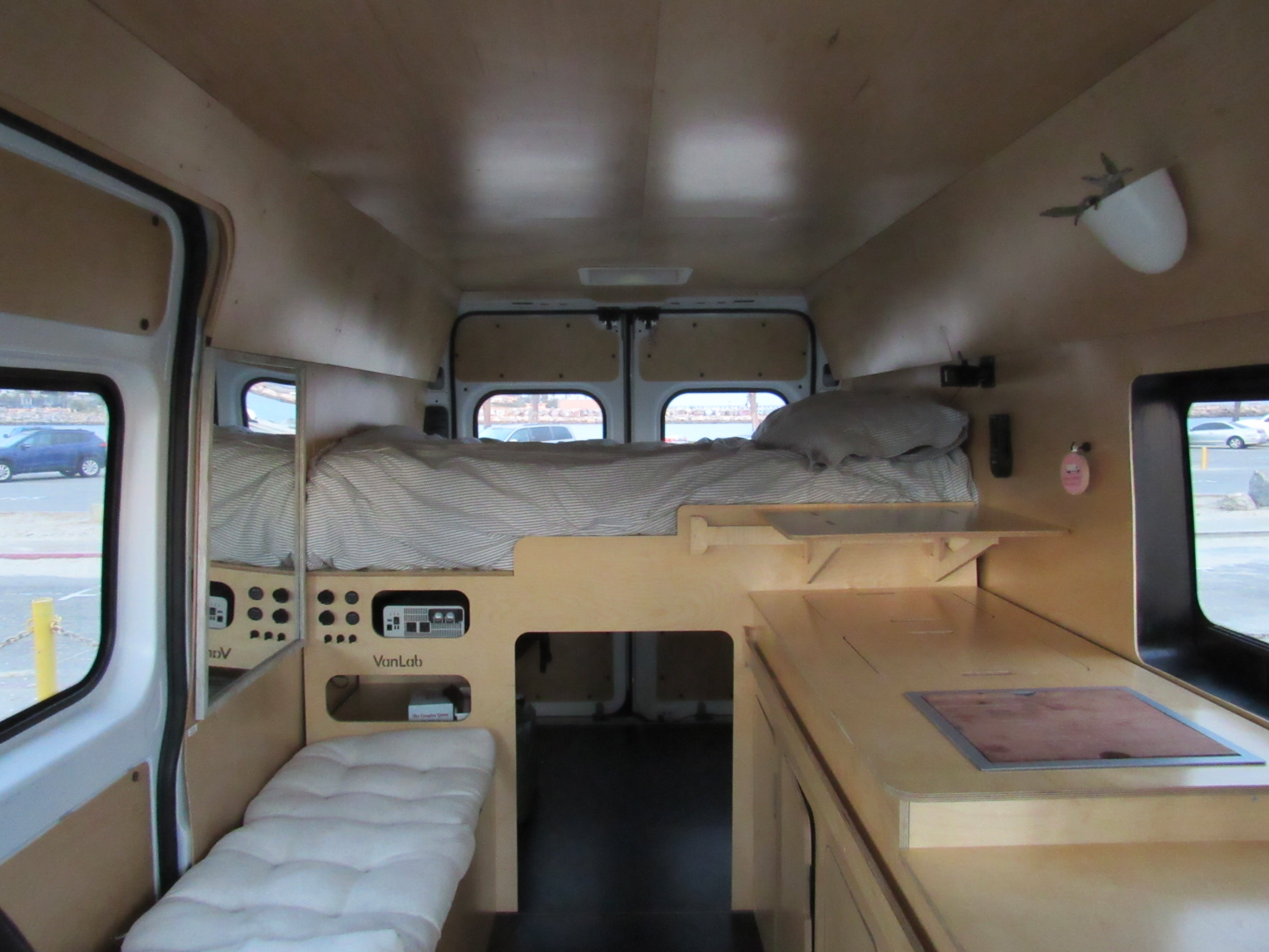 Inside this modern rv rental, a custom camper van features a bed, compact kitchen, and lounge area with light wood panels.. Dodge Promaster 2500 2023