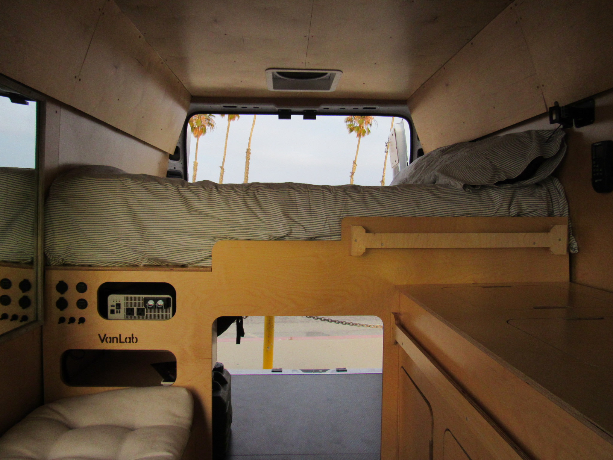 Inside a custom **rv rental** camper van: wooden interior, comfy bed, power hub, and views of palm trees.. Dodge Promaster 2500 2023